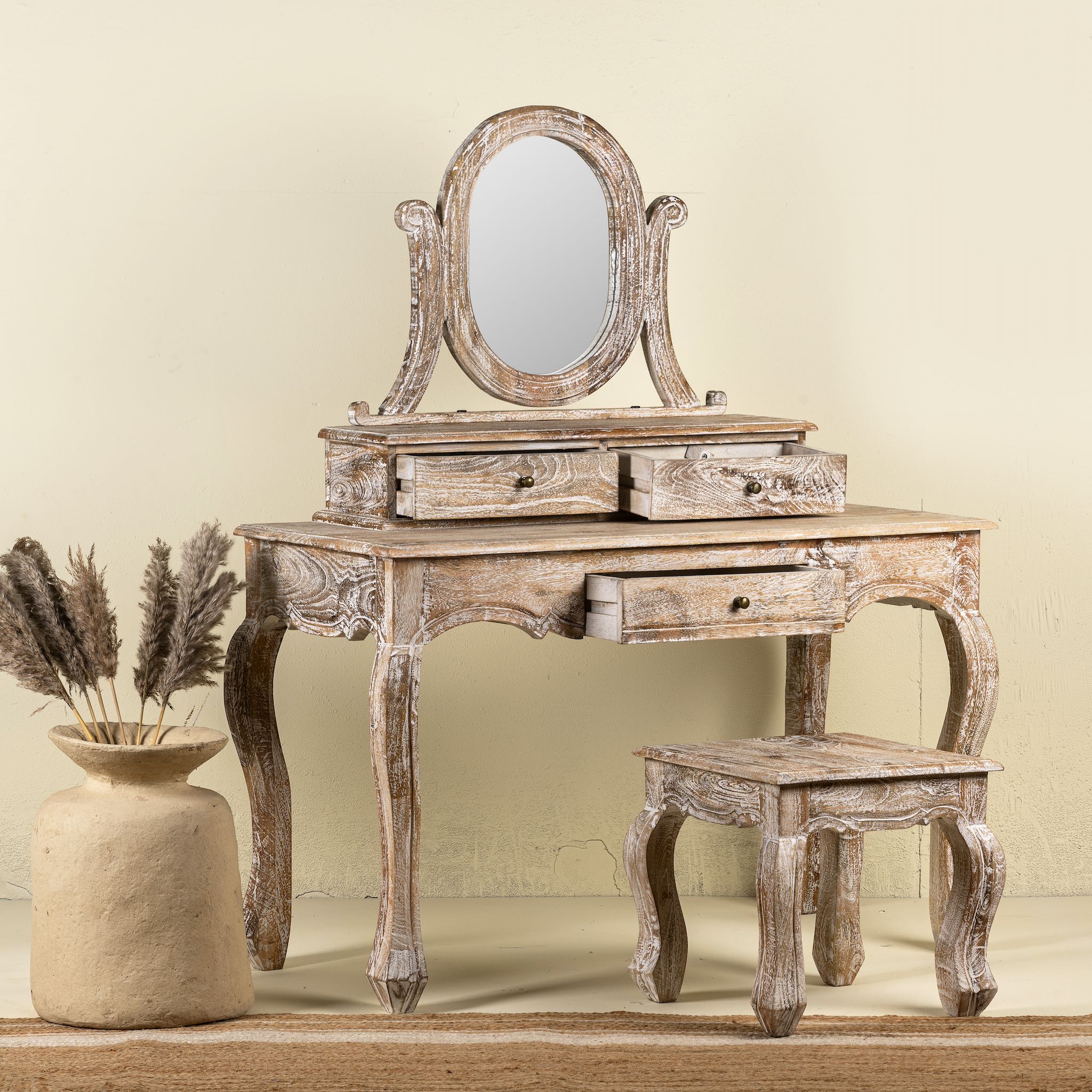 Side angle image of a handcrafted mango wood cosmetic table with a curved mirror and matching stool, showcasing a vintage style with a beige finish.
