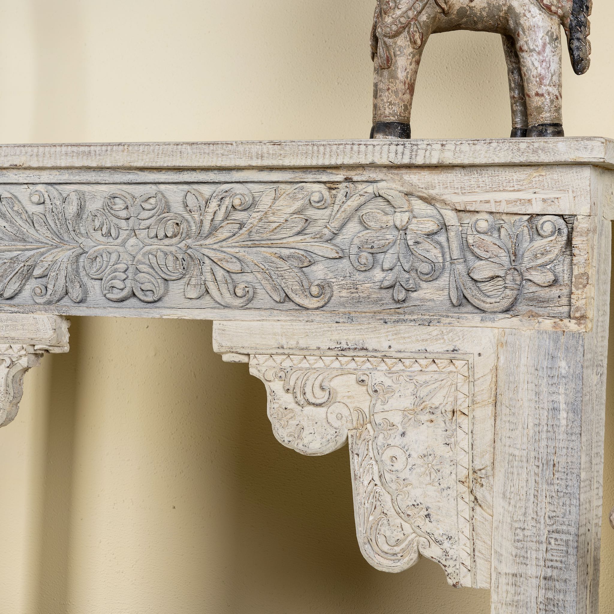 Close up side image of a handcrafted reclaimed teak wood console table with sandblasted finish, carved floral detailing, vintage corbels, and lower shelf; perfect for styling with vintage home accessories, 133 × 62 × 90 cm.