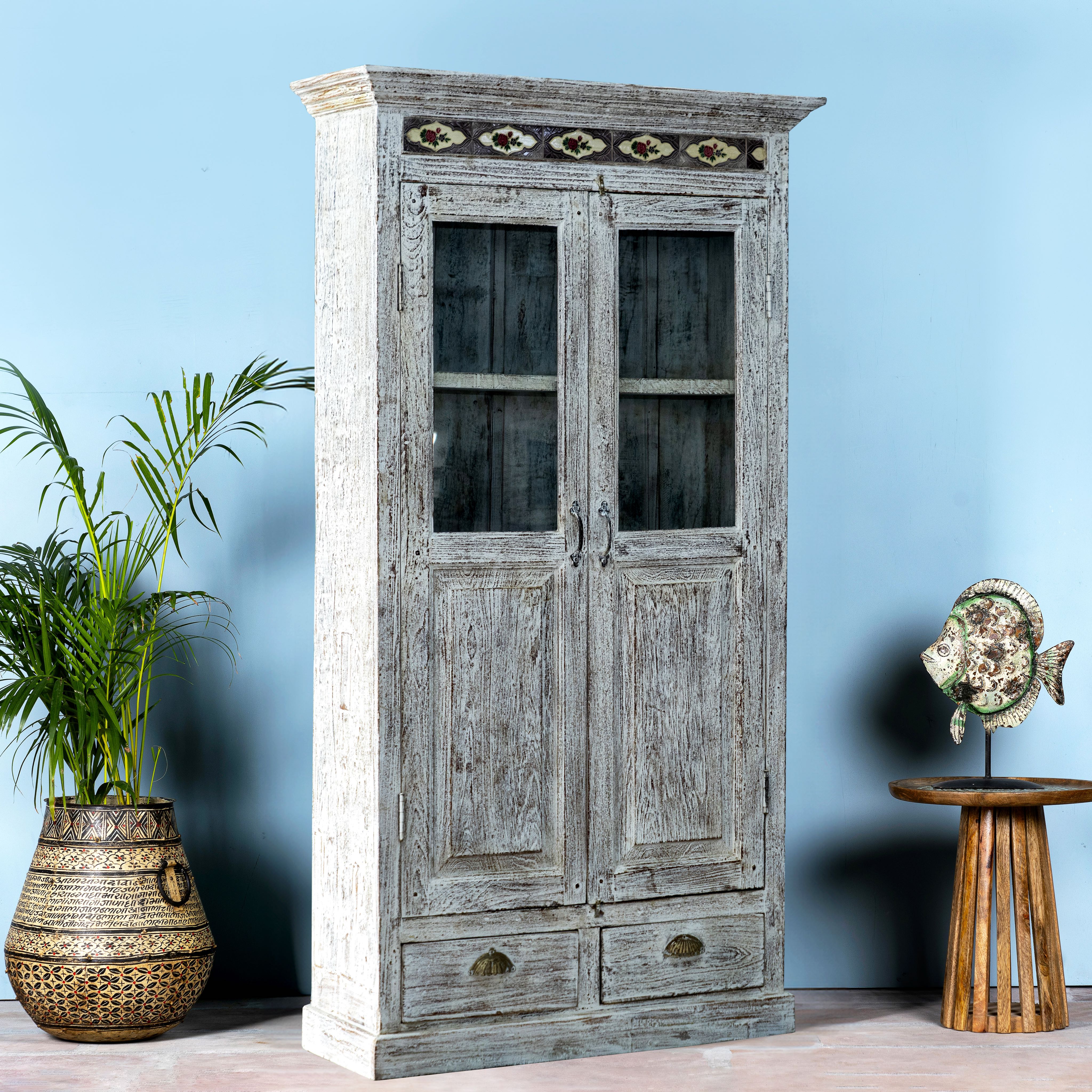 Side angle image of a reclaimed teak wood cabinet in shabby chic white with glass doors and ceramic inlays – dining room furniture with vintage elegance.