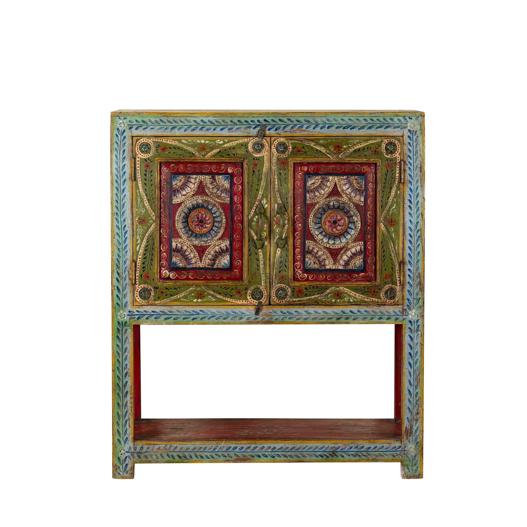 White background image of a small hand-painted console made from reclaimed wood, featuring vibrant decorative motifs in red, green, blue, and gold on double doors, with intricate floral and geometric patterns and a lower open shelf for added display.