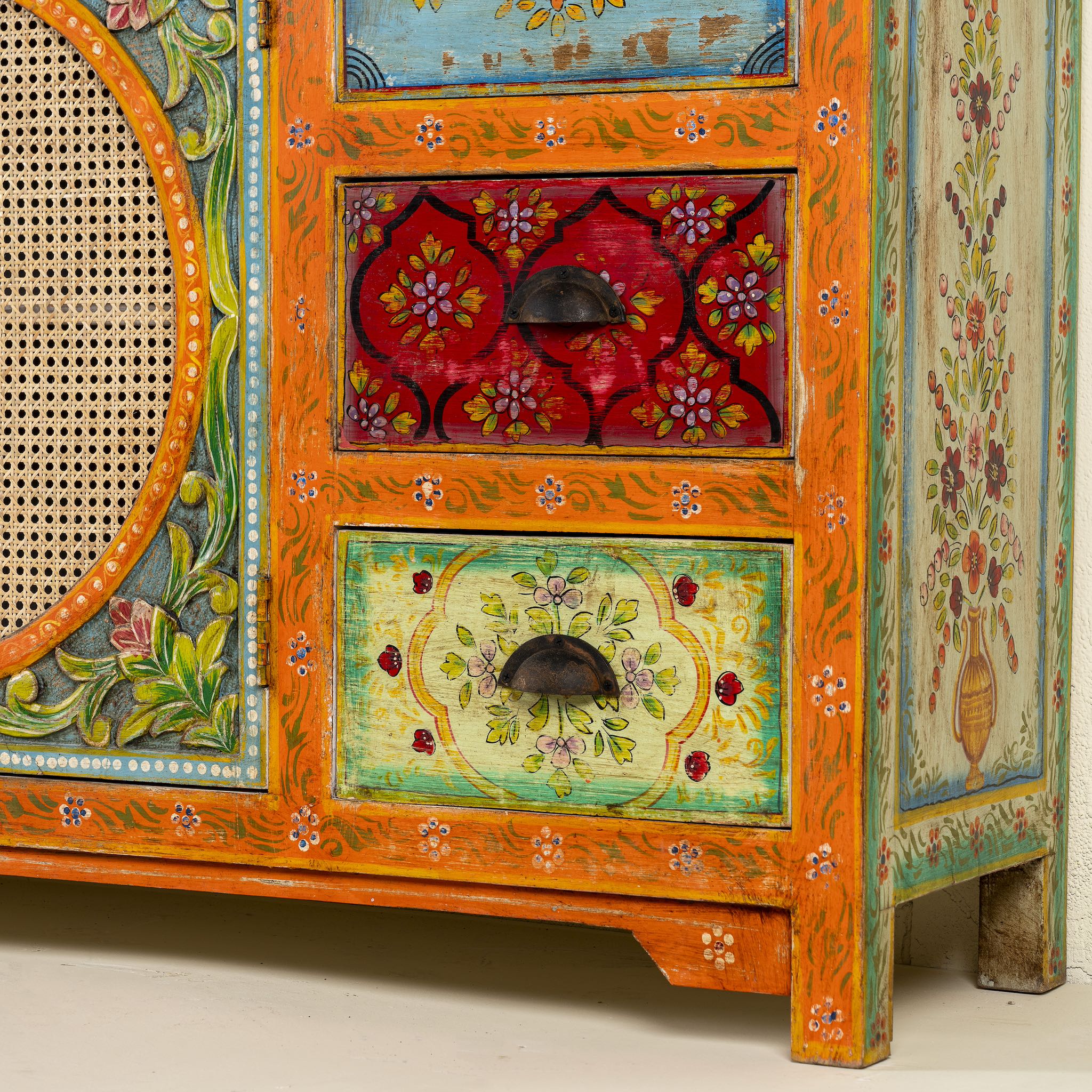 Close up of the leg part of a vintage style furniture sideboard with hand-painted floral motifs and rattan door inserts, bohemian rattan door furniture, 160 × 40 × 90 cm.