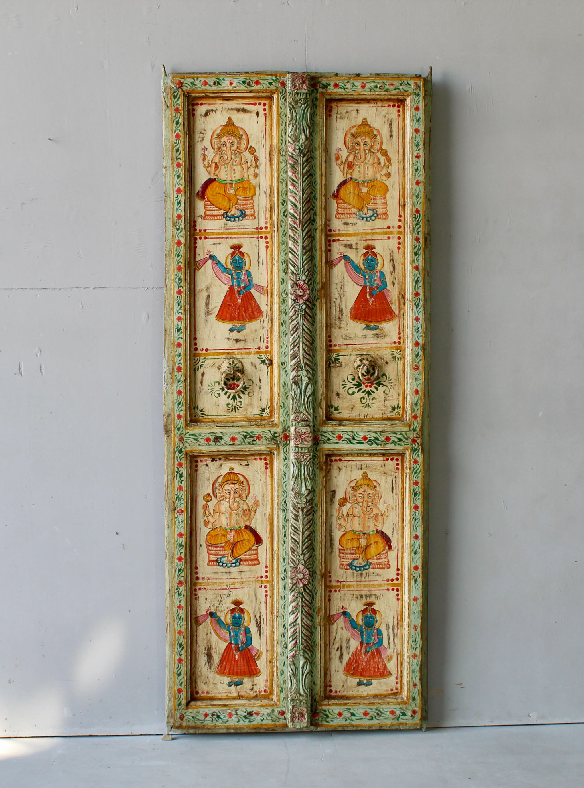 Aum hand-painted teak door panel featuring Goddess Lakshmi and traditional dancers, framed by leafy green carvings—a spiritual and unique Indian wall decoration repurposed from antique teak architecture.