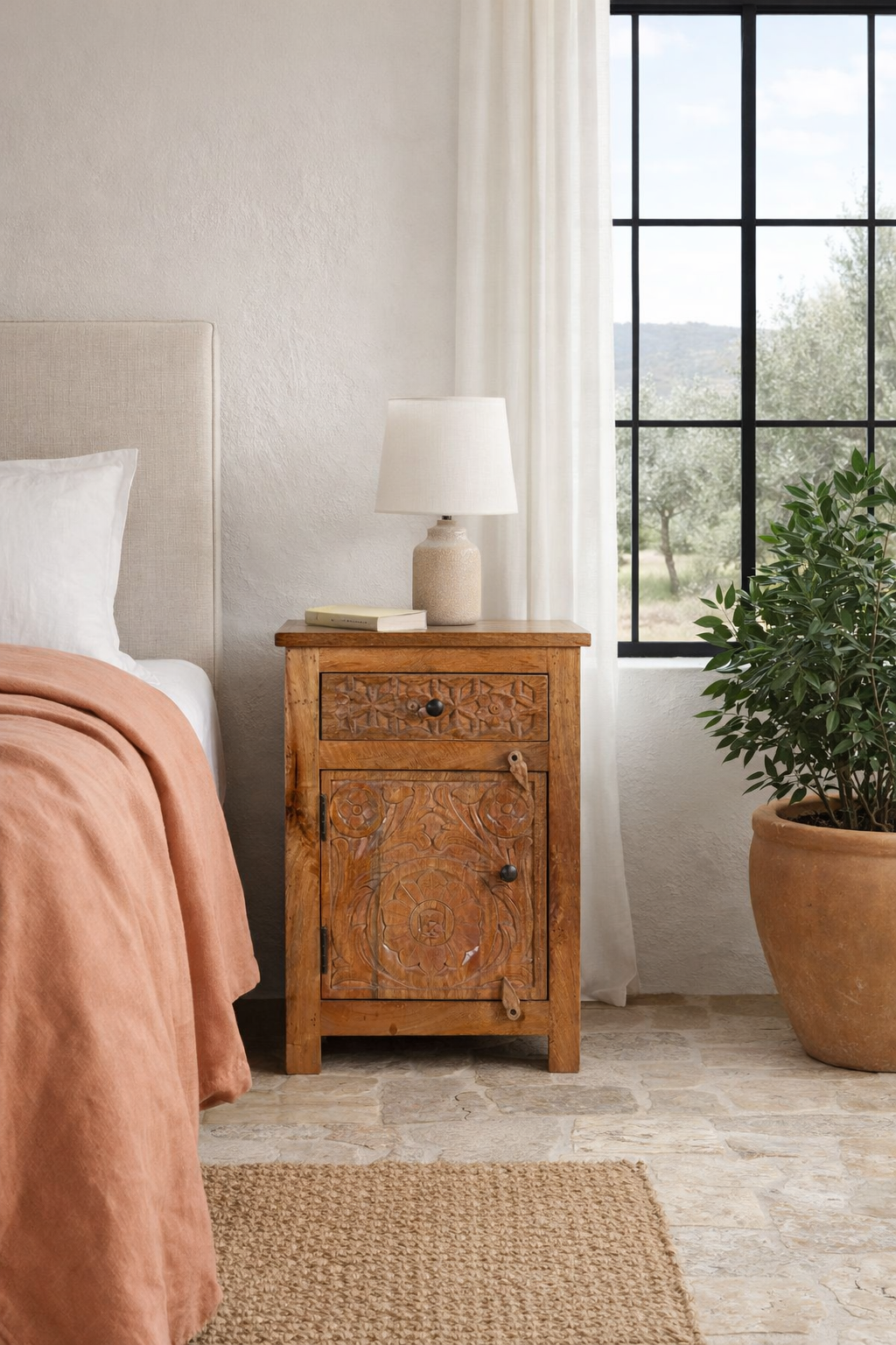 Lifestyle imagination of a pair of handcrafted bedside tables Avi made from solid mango wood, featuring floral hand-carved motifs inspired by Ibiza style. Each table includes a drawer and a cabinet, with a natural wood finish that highlights artisanal detail and organic warmth.
