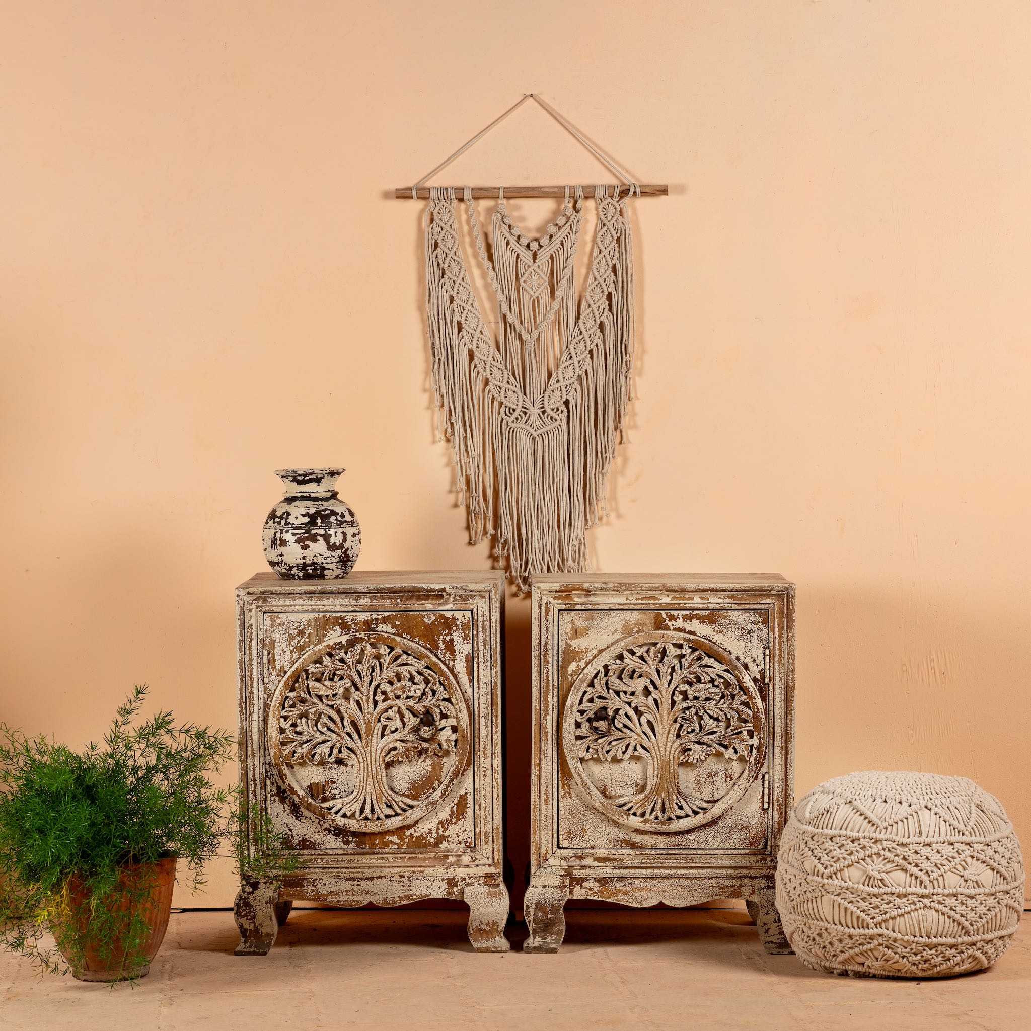 A pair of vintage design hand-carved bedside tables made from natural mango wood, with a tree motif, displayed with a rattan hanging planter and other decorative items on a neutral background.