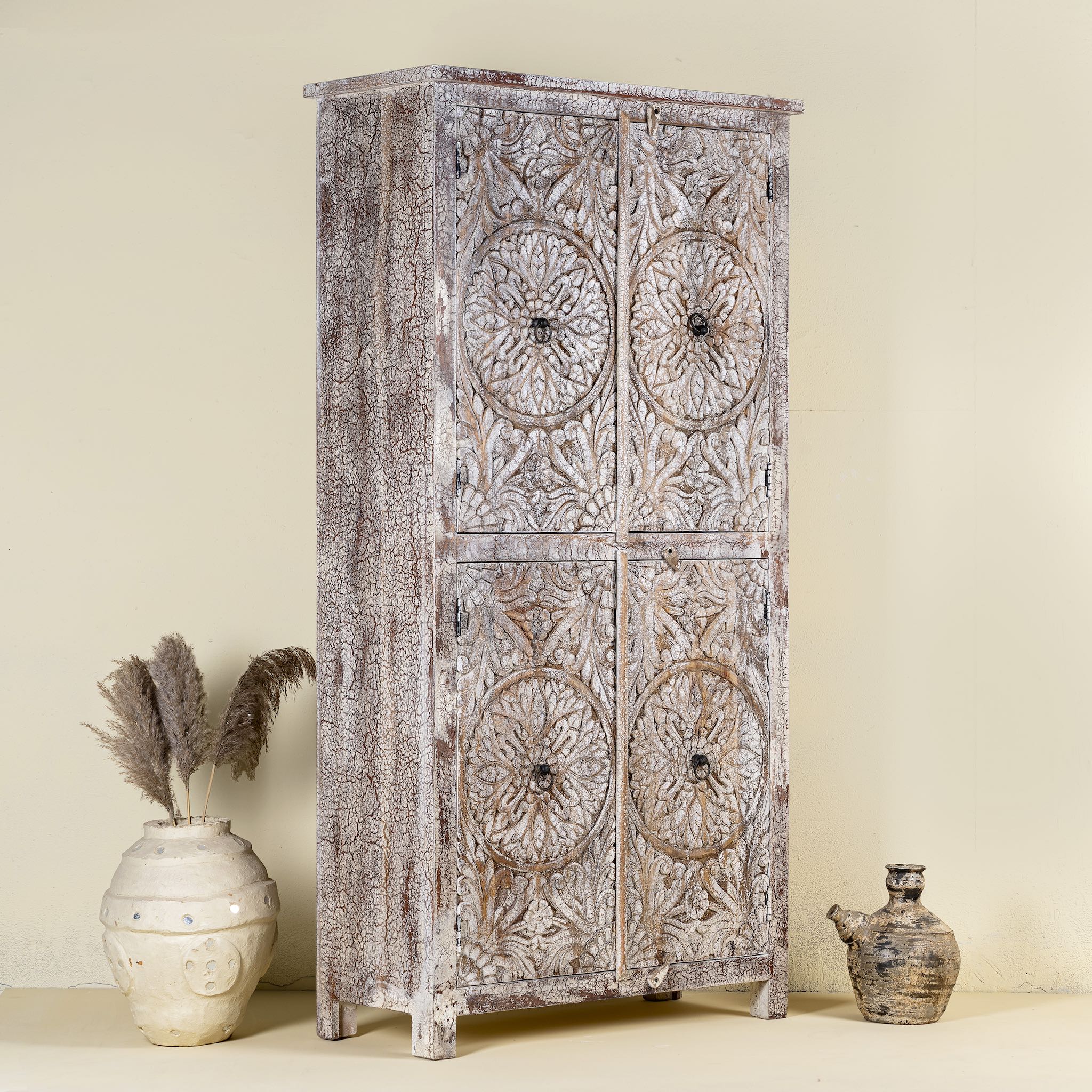 Side view of a hand-carved acacia wood wardrobe with floral detailing and distressed finish – vintage living room furniture with artisan craftsmanship.