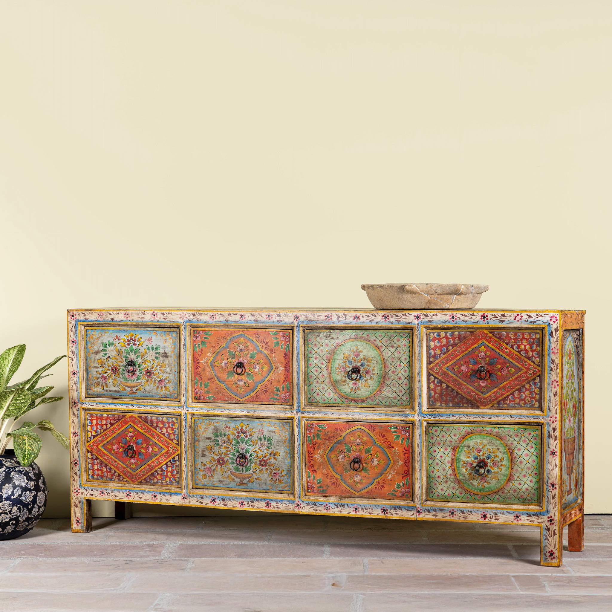 Side angle image of a hand painted sideboard with 8 drawers made of natural mango wood; artisanal chest for bohemian interior, 200 × 40 × 90 cm.