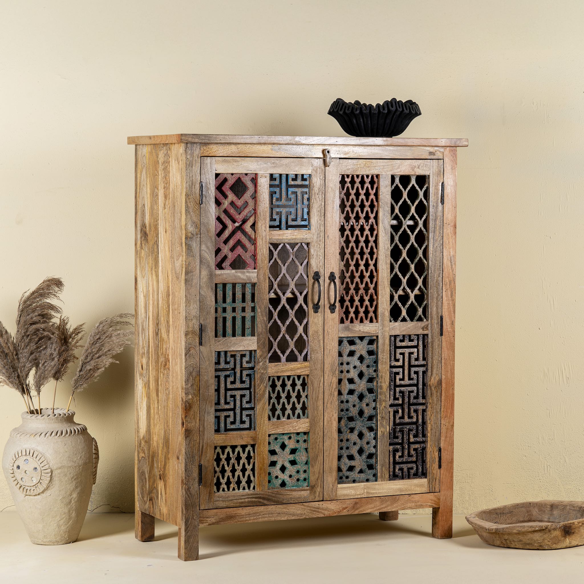 Side angle image of a artisanal mango wood cabinet with hand-carved floral and geometric lattice doors, distressed finish; ideal for boho style interiors, 100 × 45 × 130 cm.