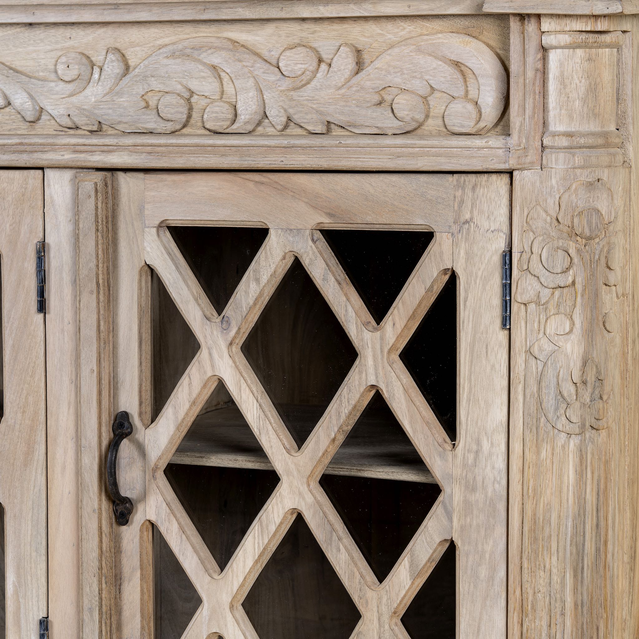 Close up image of a rustic sideboard made of Mango wood with hand-carved details and glass panelled doors featuring a diamond lattice design.