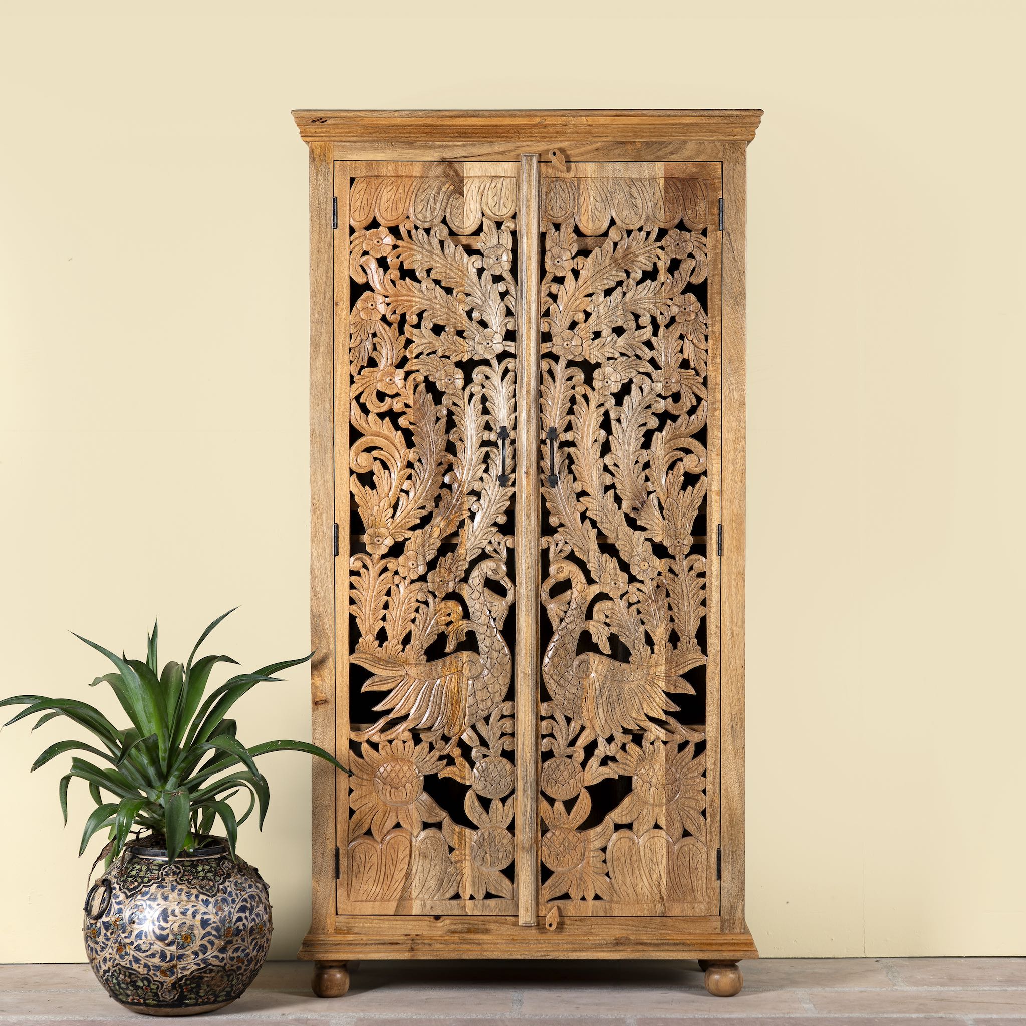 Lifestyle image of a hand-carved mango wood cupboard with Indian peacock design motifs, Mediterranean-style wardrobe; elegant mango wood furniture, 190 × 100 × 40 cm.