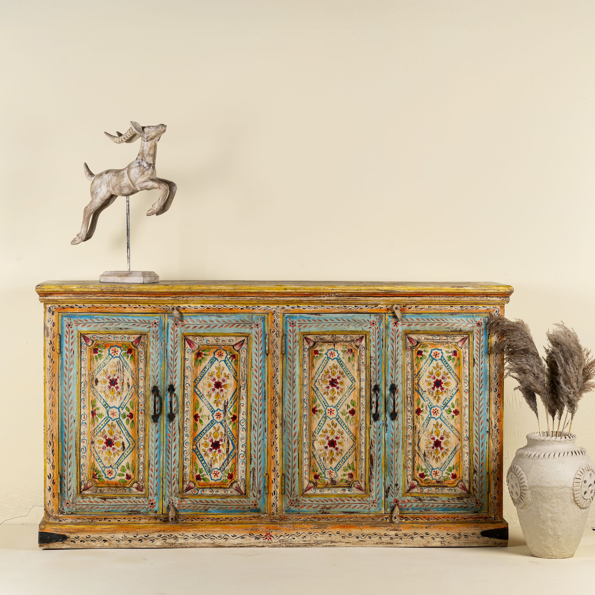 Front view image of a hand-painted sideboard made from reclaimed wood, featuring four intricately detailed doors with vibrant floral and geometric motifs in soft blues, yellows, and reds, finished with a distressed vintage patina for a charming, artisanal look.