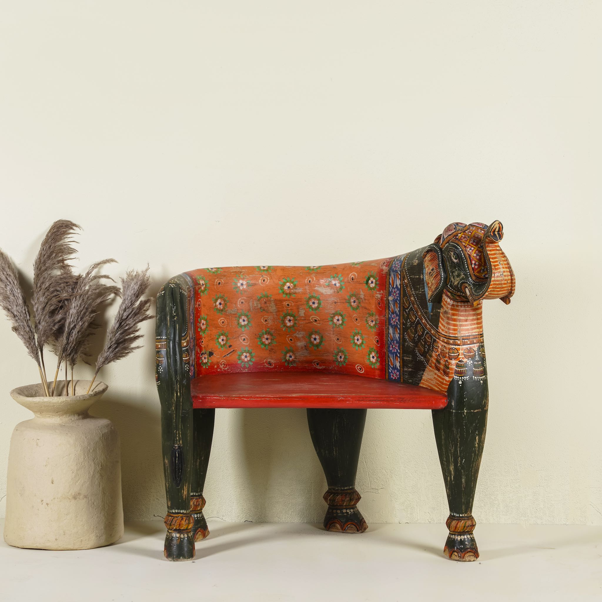 Elephant-shaped armchair crafted from reclaimed wood, featuring intricate hand-painted details in vibrant red, orange, green, and multi coloured floral patterns, with sculpted elephant head and legs for a whimsical, artistic touch.