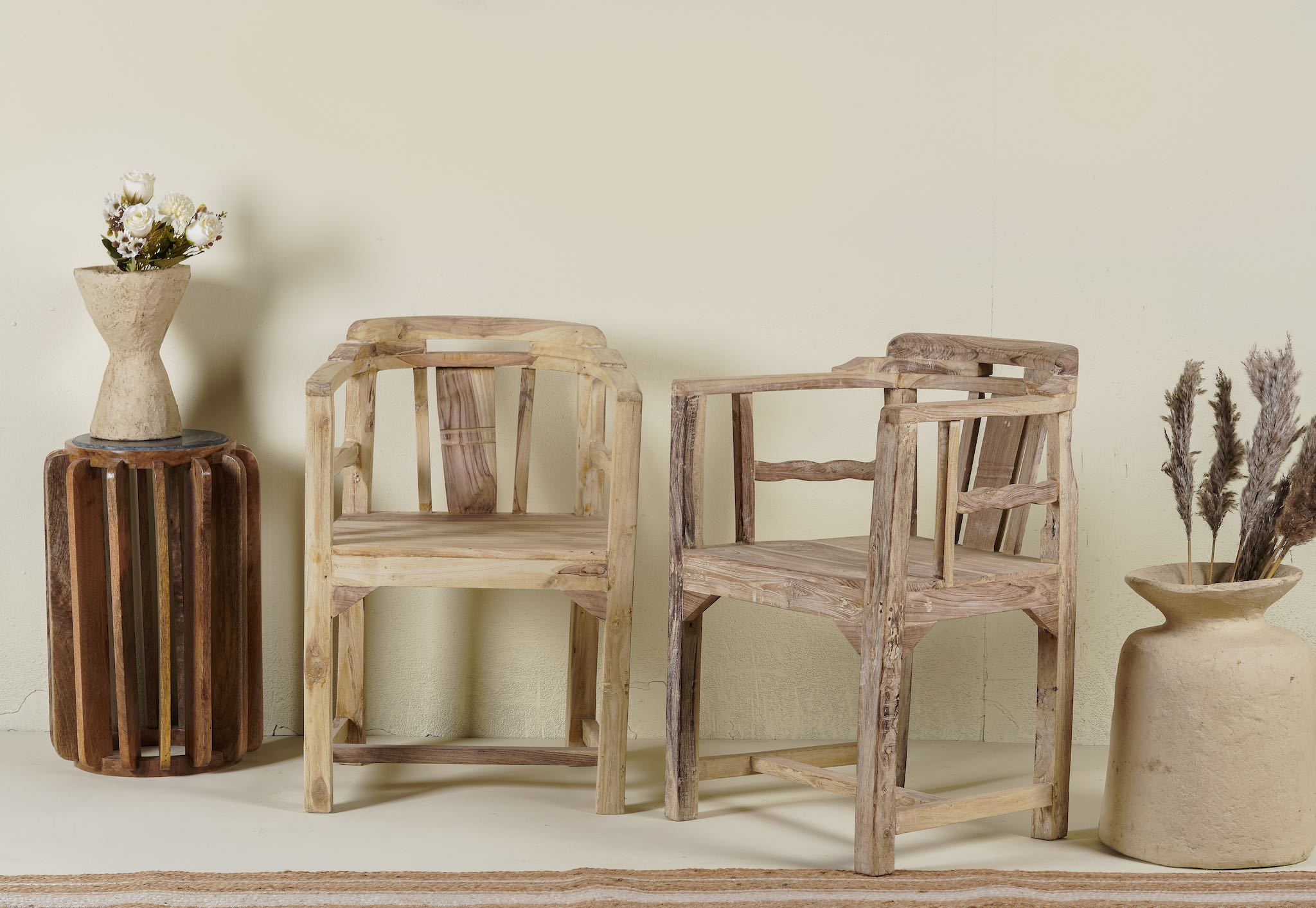 Side angle of of a rustic-style armchair made from reclaimed teak wood, featuring a natural, unfinished look with visible wood grain and variations in tone, and a curved backrest with vertical slats.