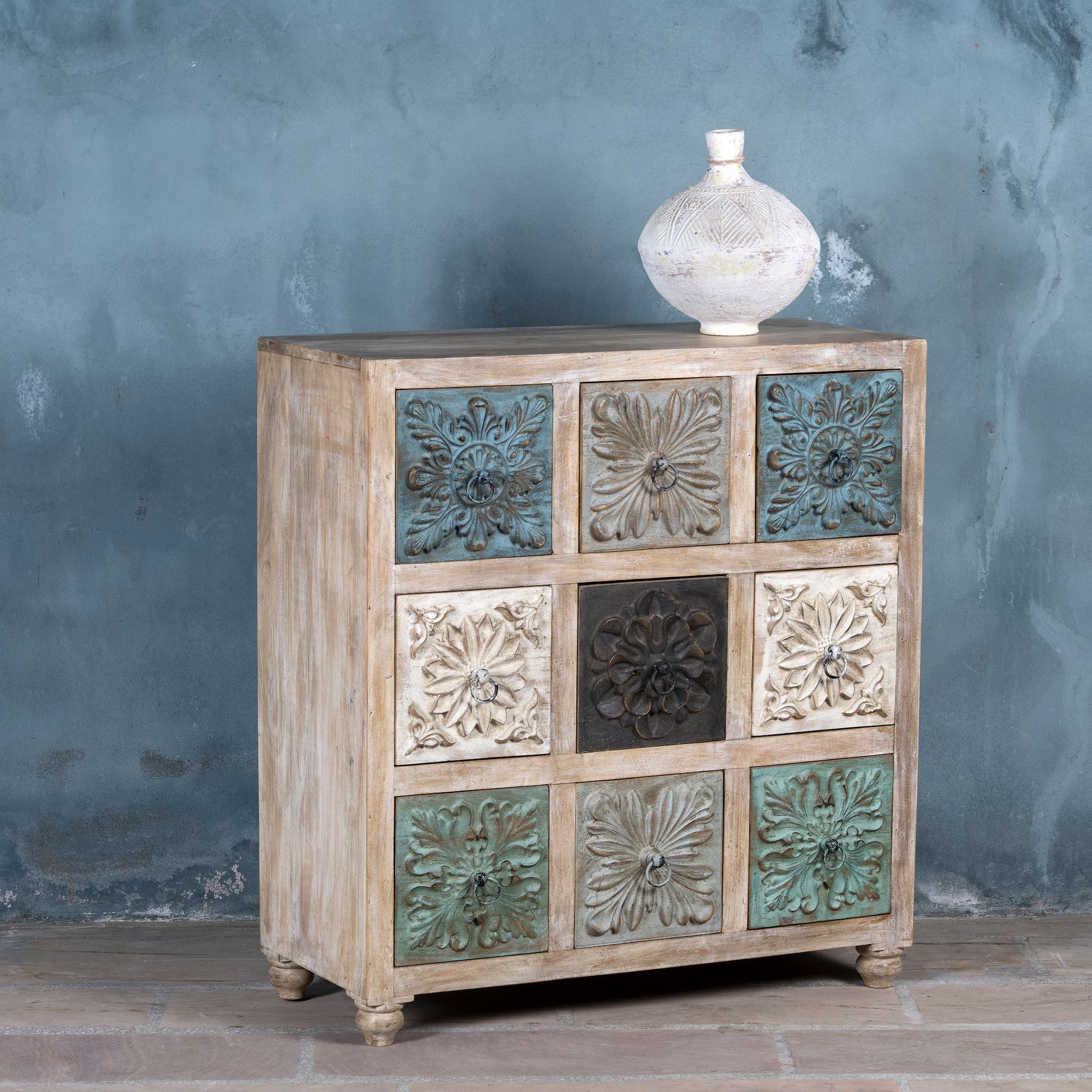 Side angle image of a mango wood chest of drawers Hansika with nine hand-carved floral drawer fronts in soft bohemian colours. A unique carved sideboard combining artisan design with versatile storage.