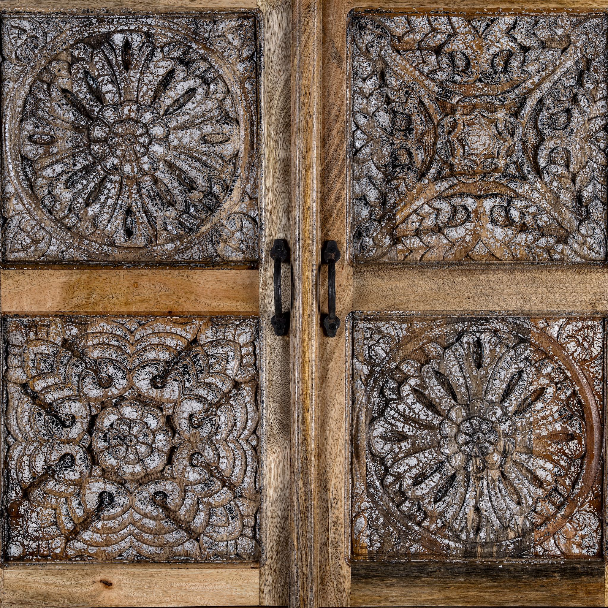 Close up view of a hand-carved mango wood cabinet with floral motifs and silver finish – bedroom furniture with rustic charm and artisanal detail.