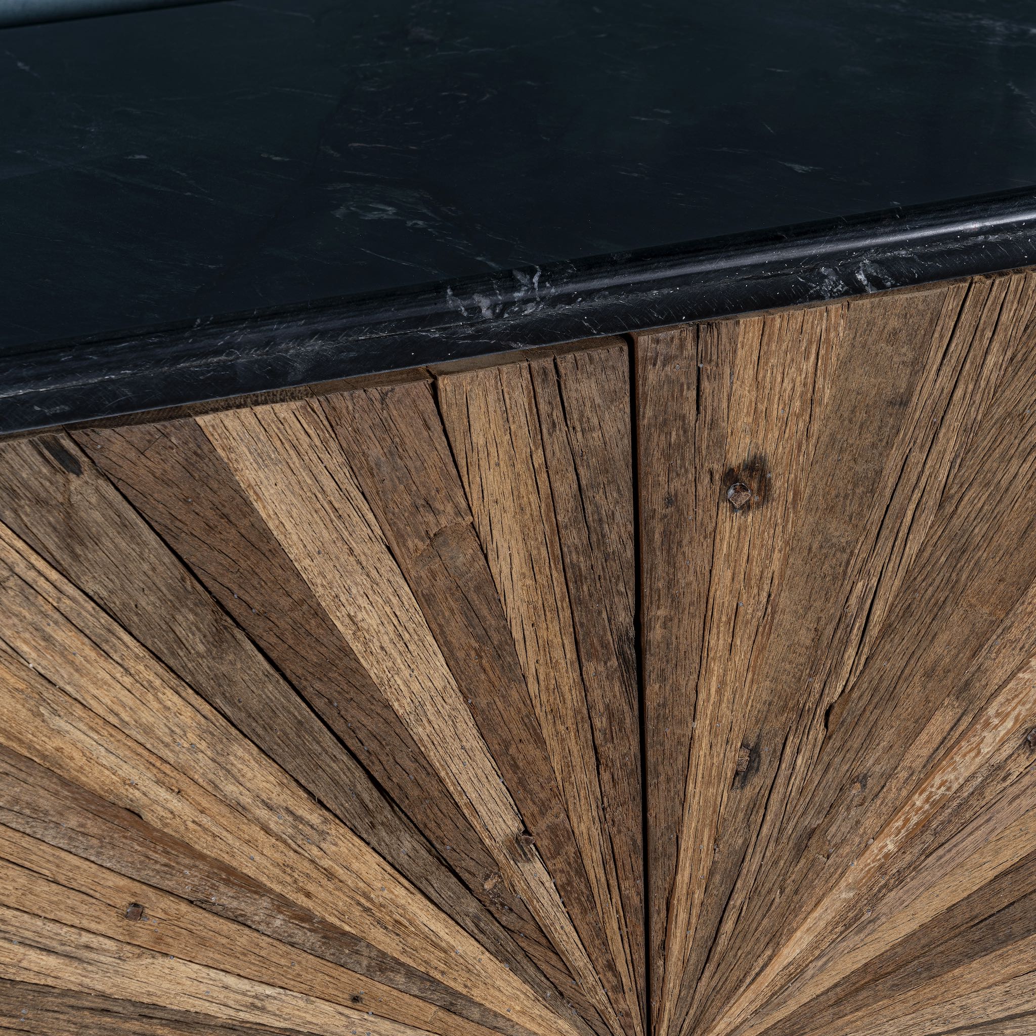 Close up of the marble top of a reclaimed wood sideboard with sunburst carved doors, sliding black marble top, and rustic finish, ideal for rustic interior design.
