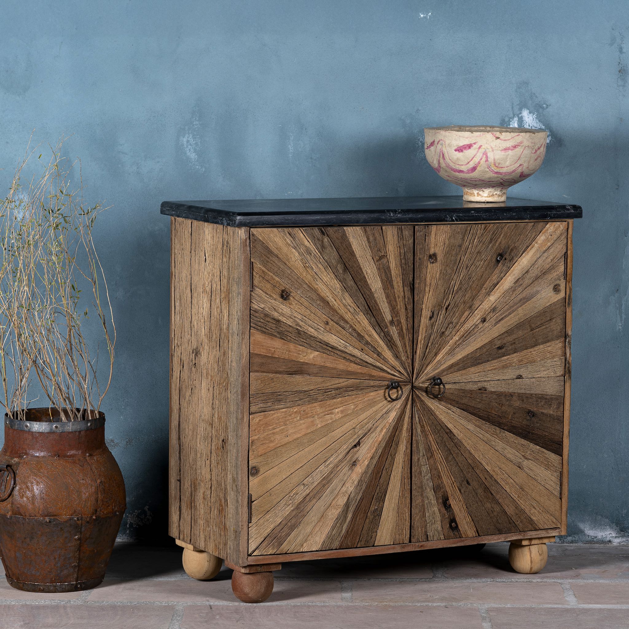Side angle image of a reclaimed wood sideboard with sunburst carved doors, sliding black marble top, and rustic finish, ideal for rustic interior design.