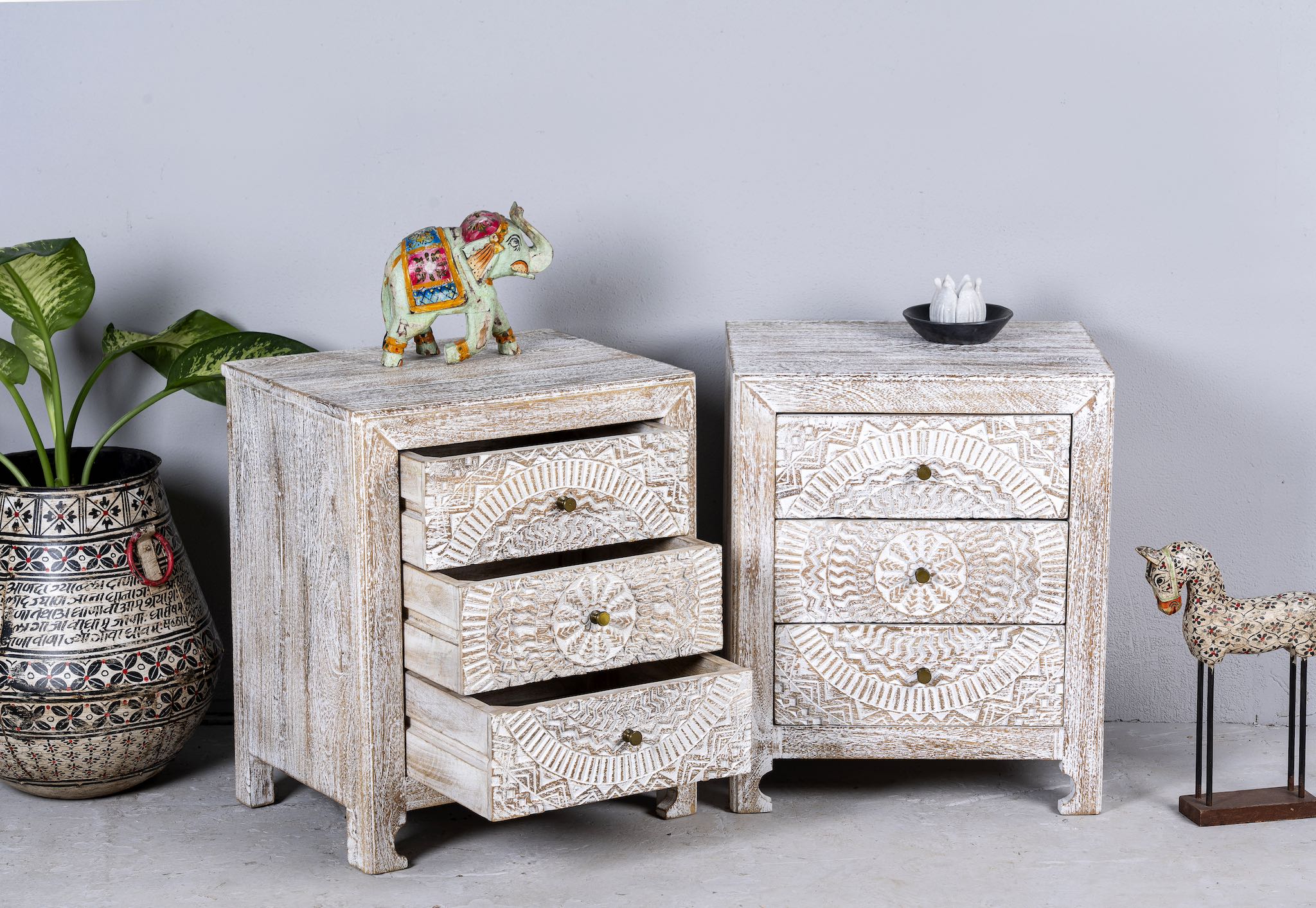 Side angle with open drawers of a set of two hand carved night stands in solid mango wood with mandala motifs; white washed furniture, 50 × 40 × 60 cm.