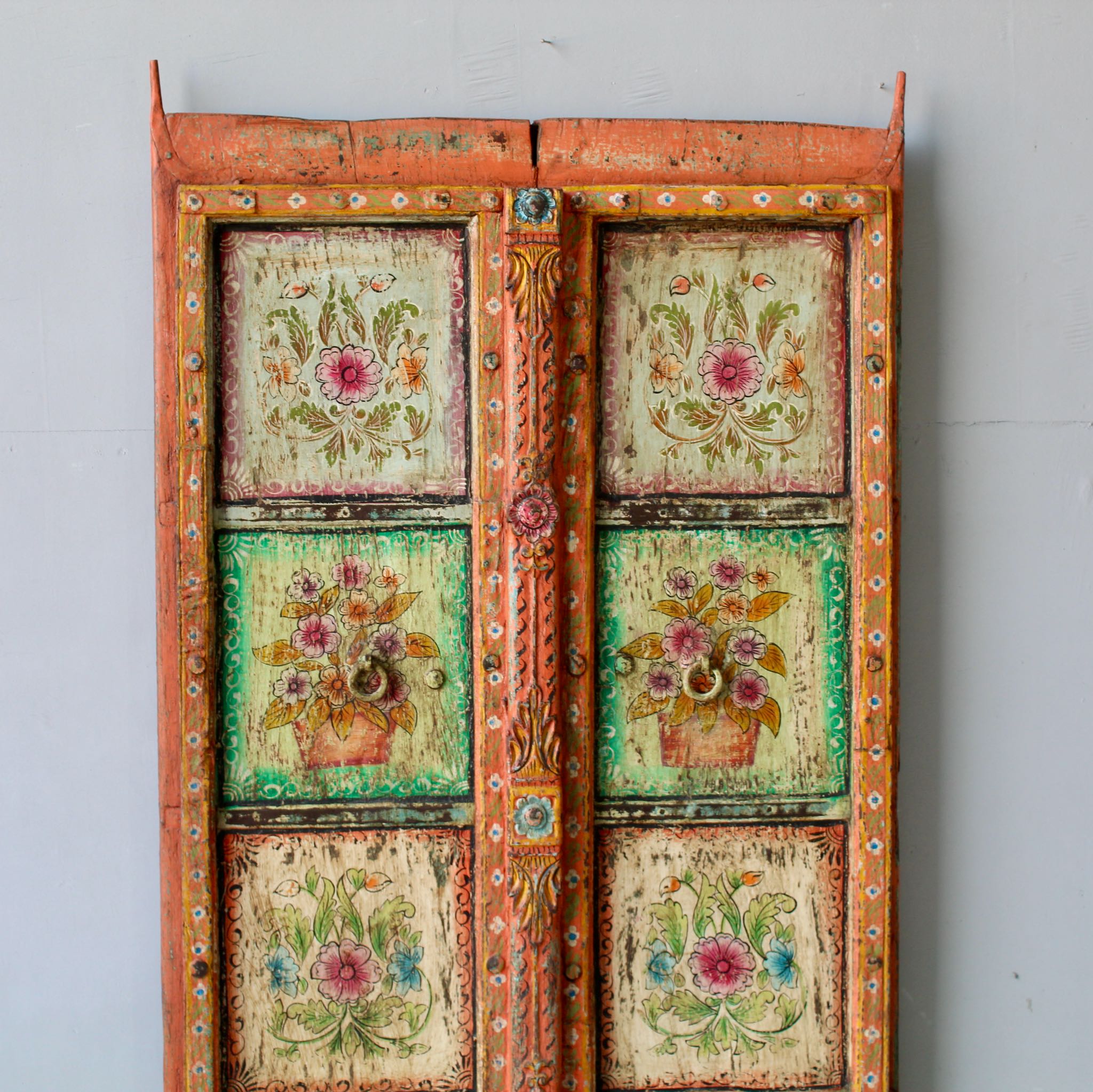 Close up image of a hand-painted antique teak wood Indian door with floral motifs, rustic orange frame, reclaimed wood vintage wall panels for bohemian and vintage home decor.