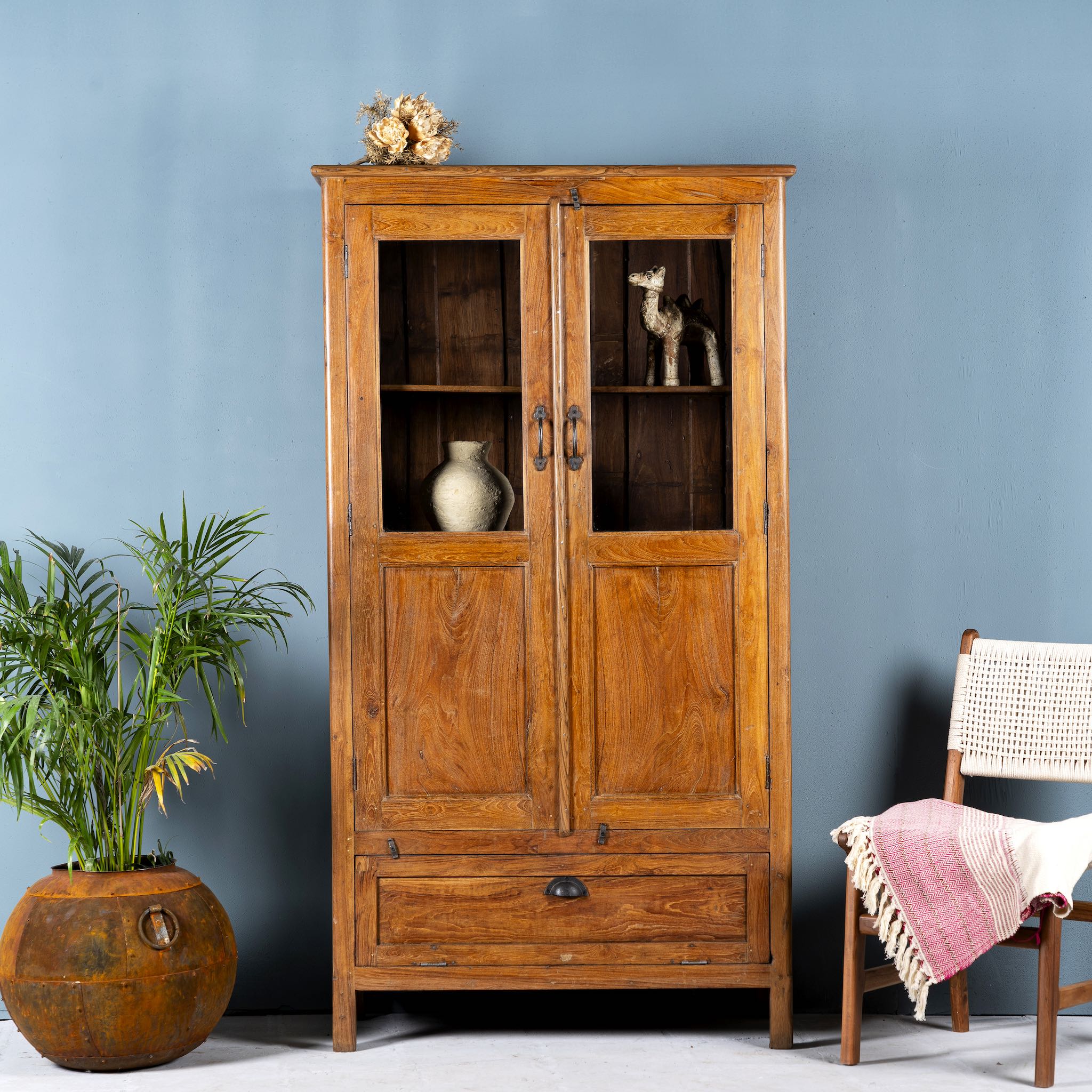 Tall reclaimed teak wood display cabinet with two glass doors and a bottom drawer – wooden display cabinet crafted as sustainable furniture with natural elegance.