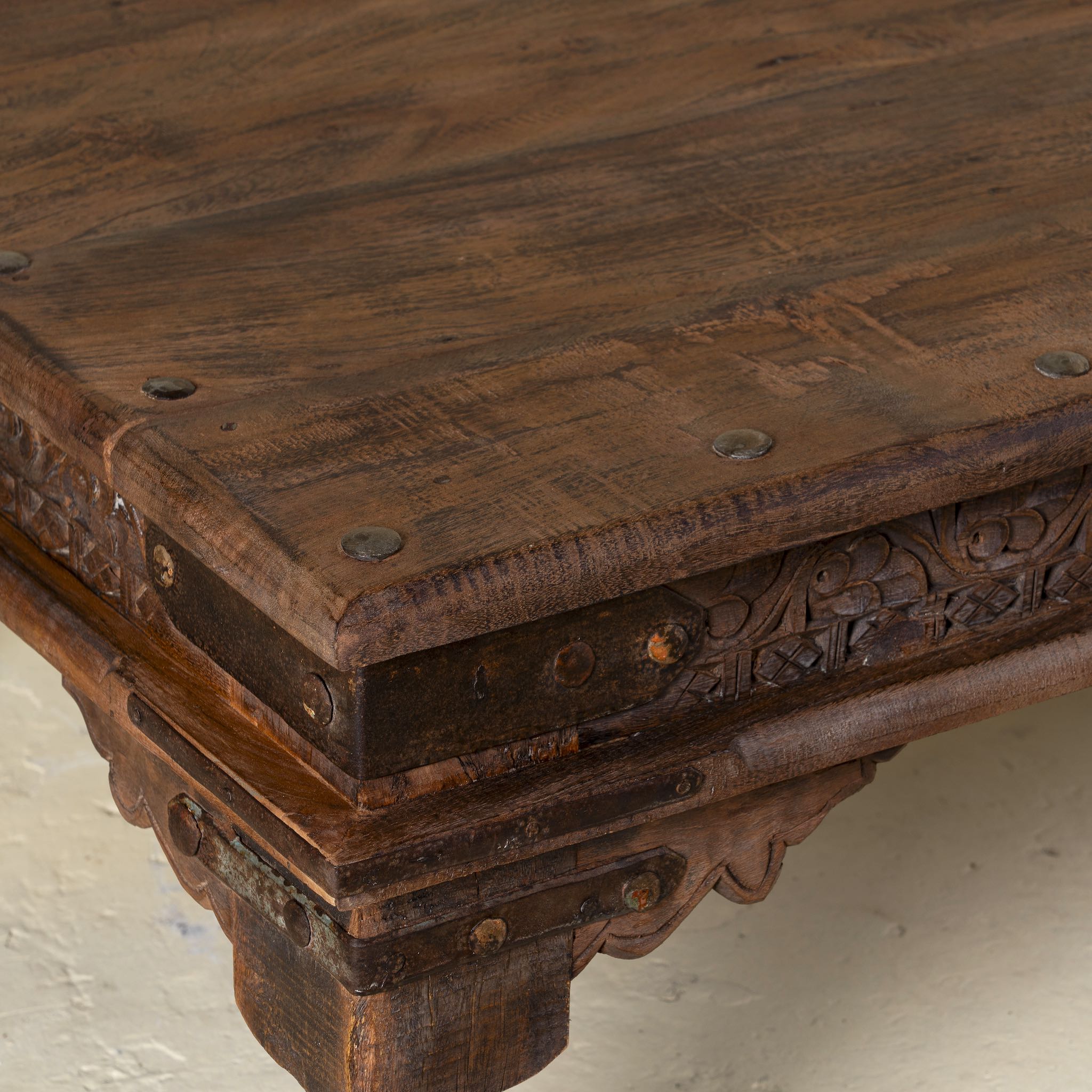 Close-up image of a rectangular teak wood coffee table with hand-carved Indian detailing, reclaimed wood finish, and iron accents; 158 × 76 × 46 cm.
