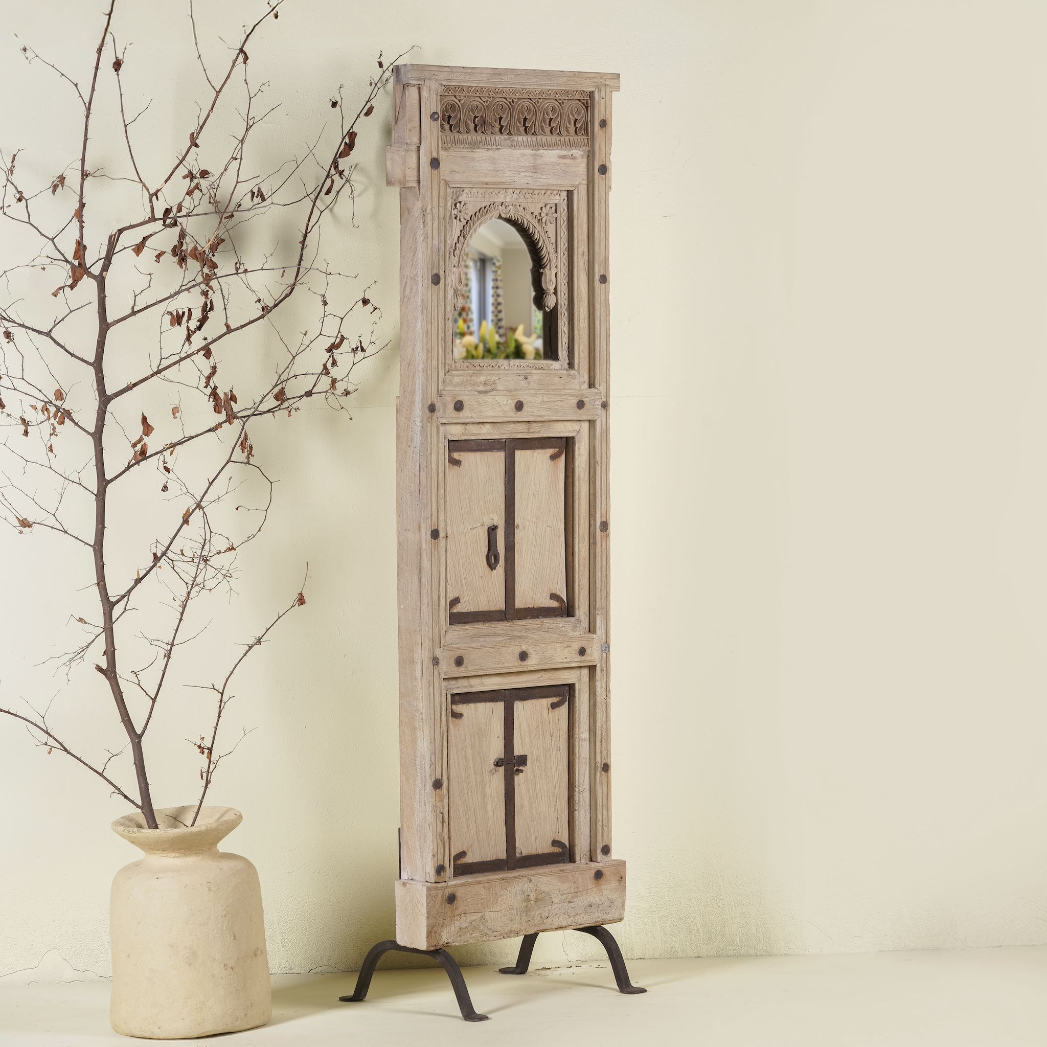 Side angle image of a mirror stand crafted from reclaimed teak wood with intricate carved detailing and two storage cabinets, set on a sturdy iron base, blending rustic charm with vintage Indian architectural elements.