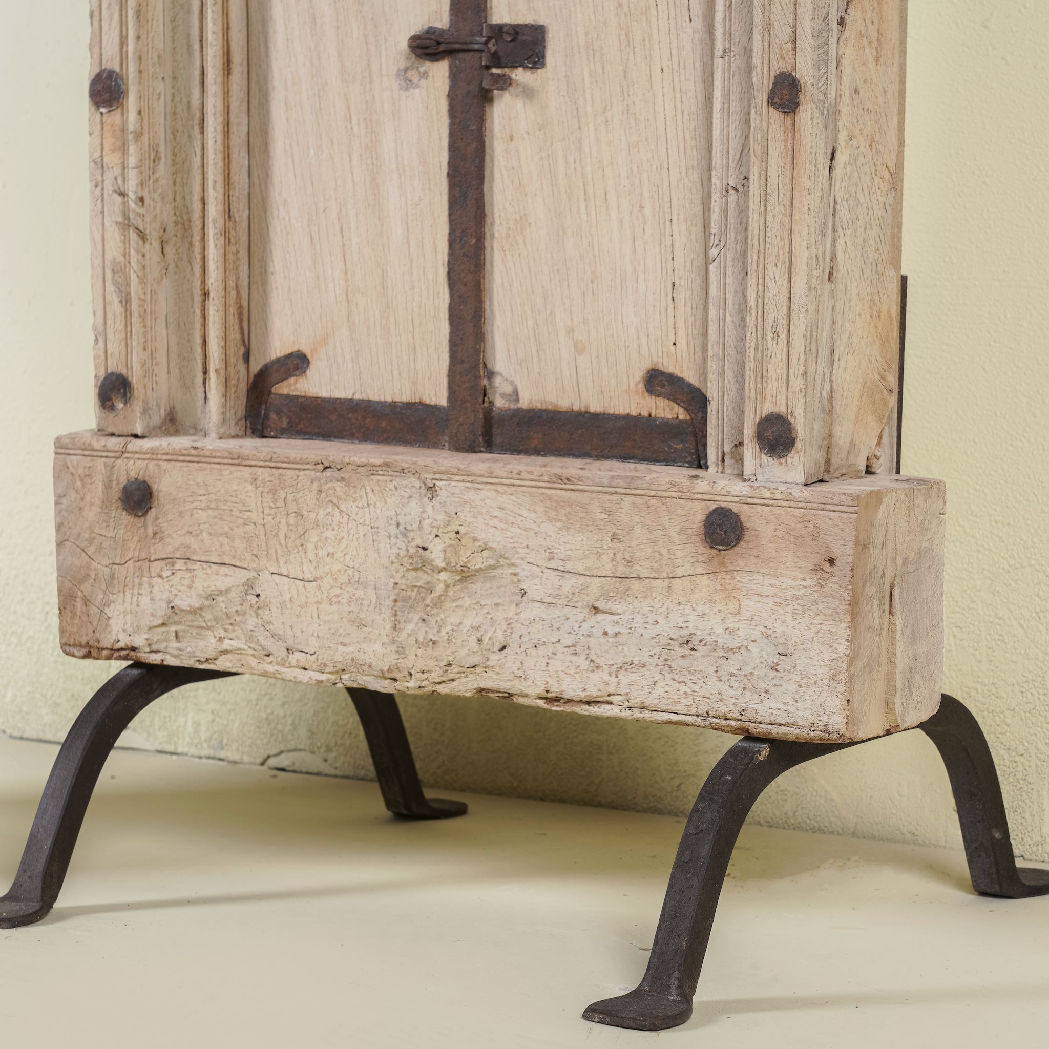 Close up of the iron stand of a mirror stand crafted from reclaimed teak wood with intricate carved detailing and two storage cabinets, set on a sturdy iron base, blending rustic charm with vintage Indian architectural elements.