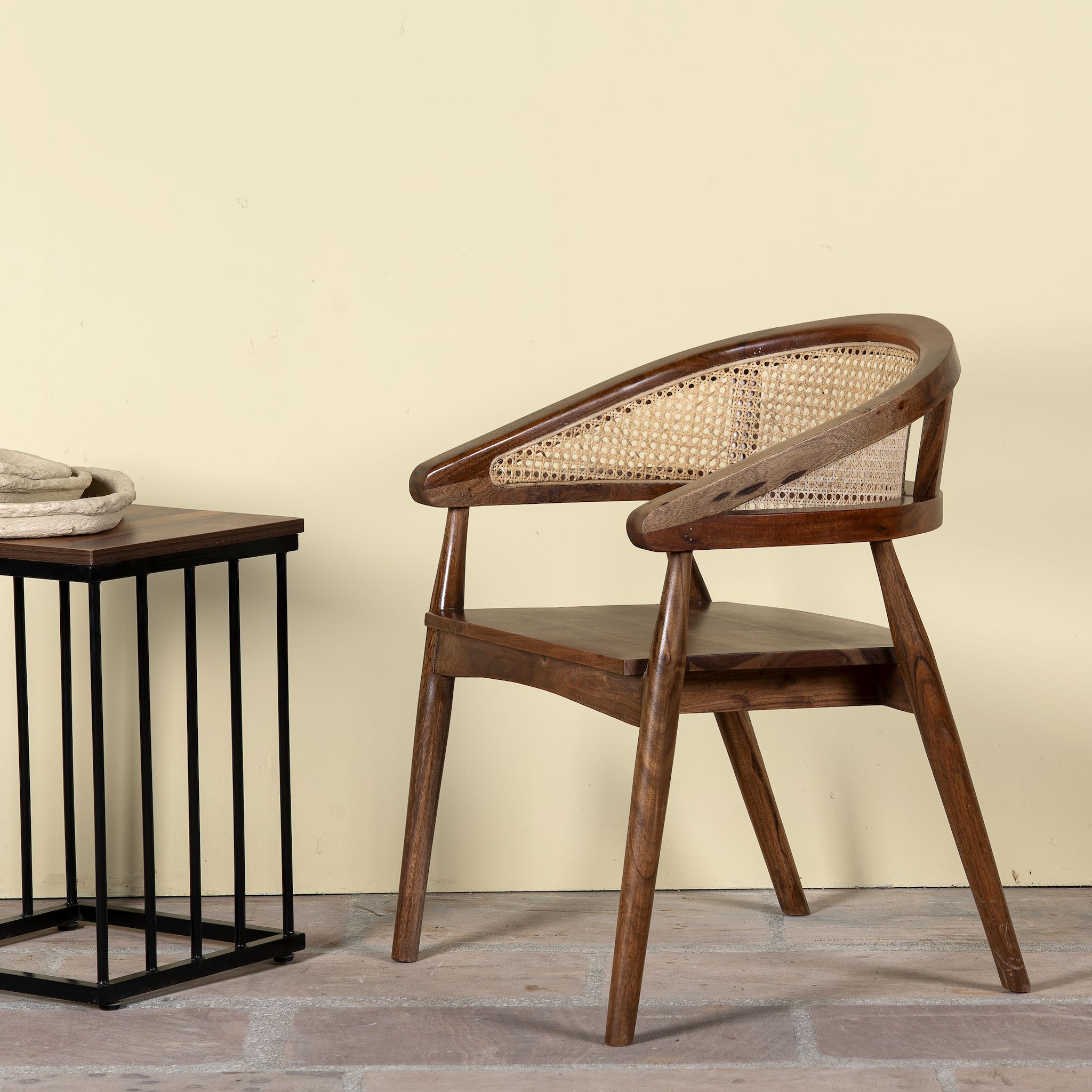 Lifestyle image of an acacia wood chair with curved frame and woven rattan backrest, elegant wooden armchair, 60 × 45 × 90 cm.