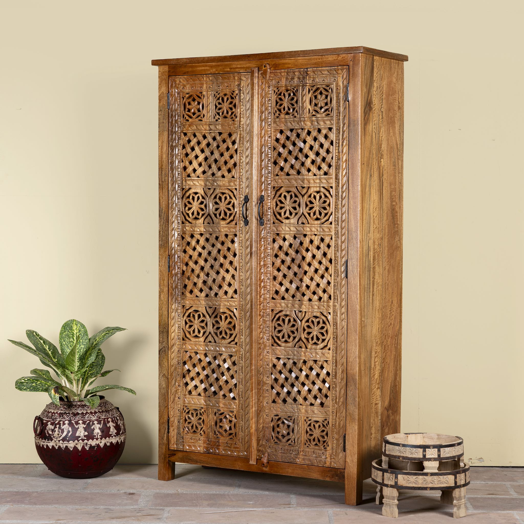 Side angle image of a hand-carved mango wood wardrobe with floral and lattice motifs – a detailed piece of carved wood furniture ideal for natural mango wood interiors.