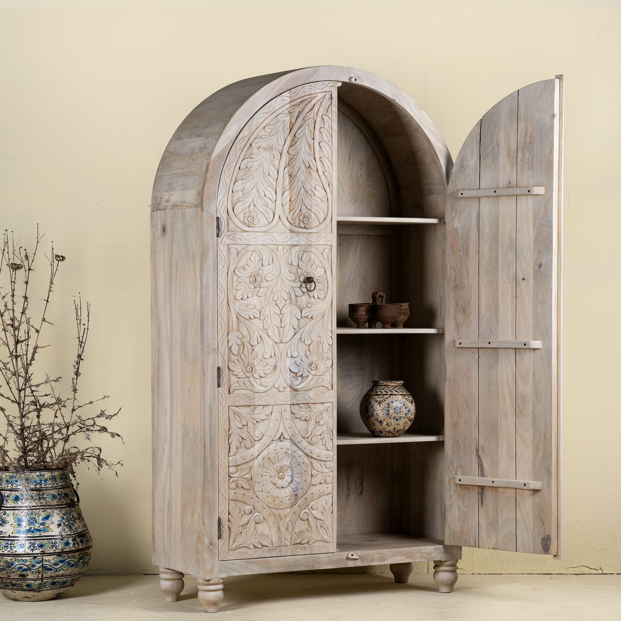 Open door image of a handcrafted mango wood wardrobe with arched top and floral carving – Tamia by Om Home & Garden, unique furniture with Ibiza-style charm for living rooms and bedrooms.