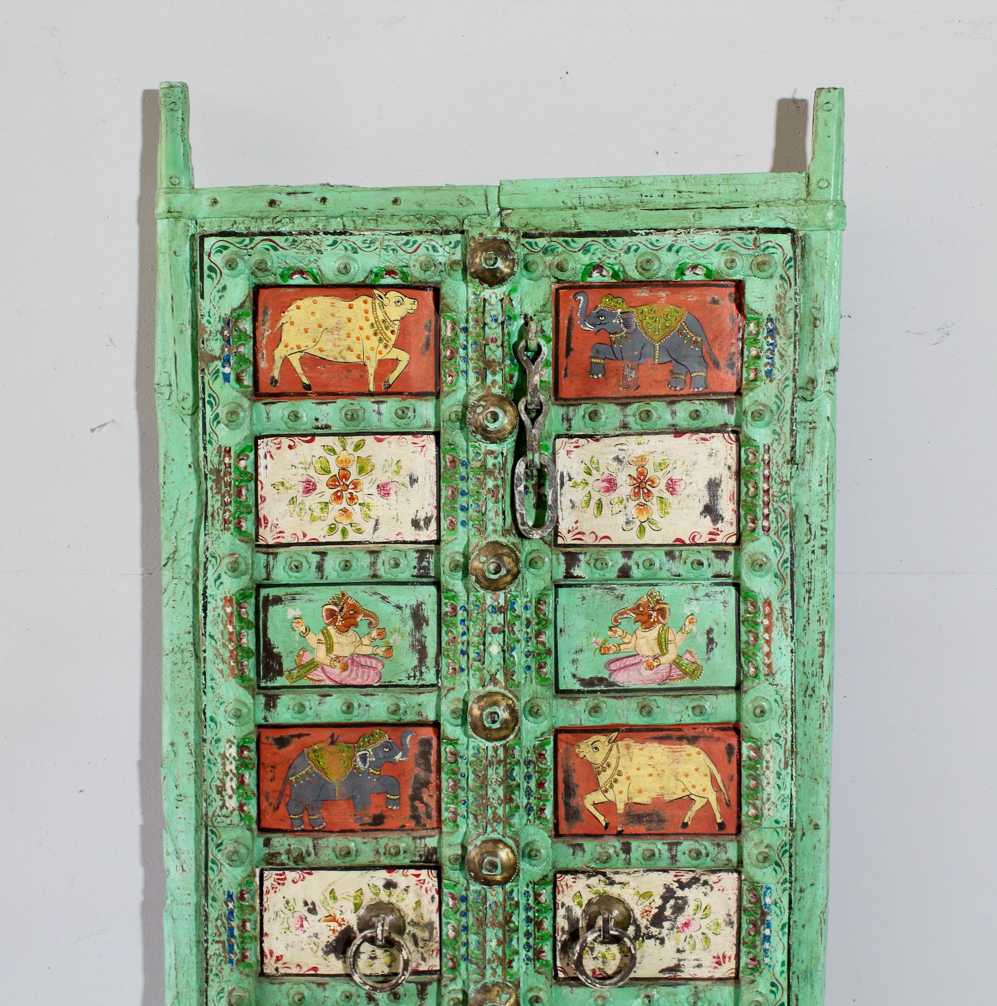 Close up image of a vintage Indian antique door panel in distressed teal with hand-painted sacred and floral motifs, repurposed as wall art and vintage home decor.