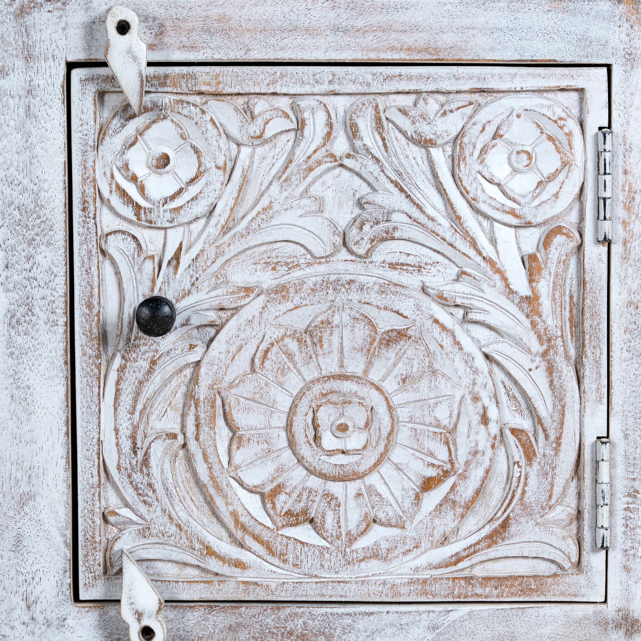 Close up image of a pair of mango wood nightstands Uday with whitewashed vintage finish, featuring hand-carved geometric and floral designs. Each bedside table includes a drawer and cabinet for elegant and practical storage.