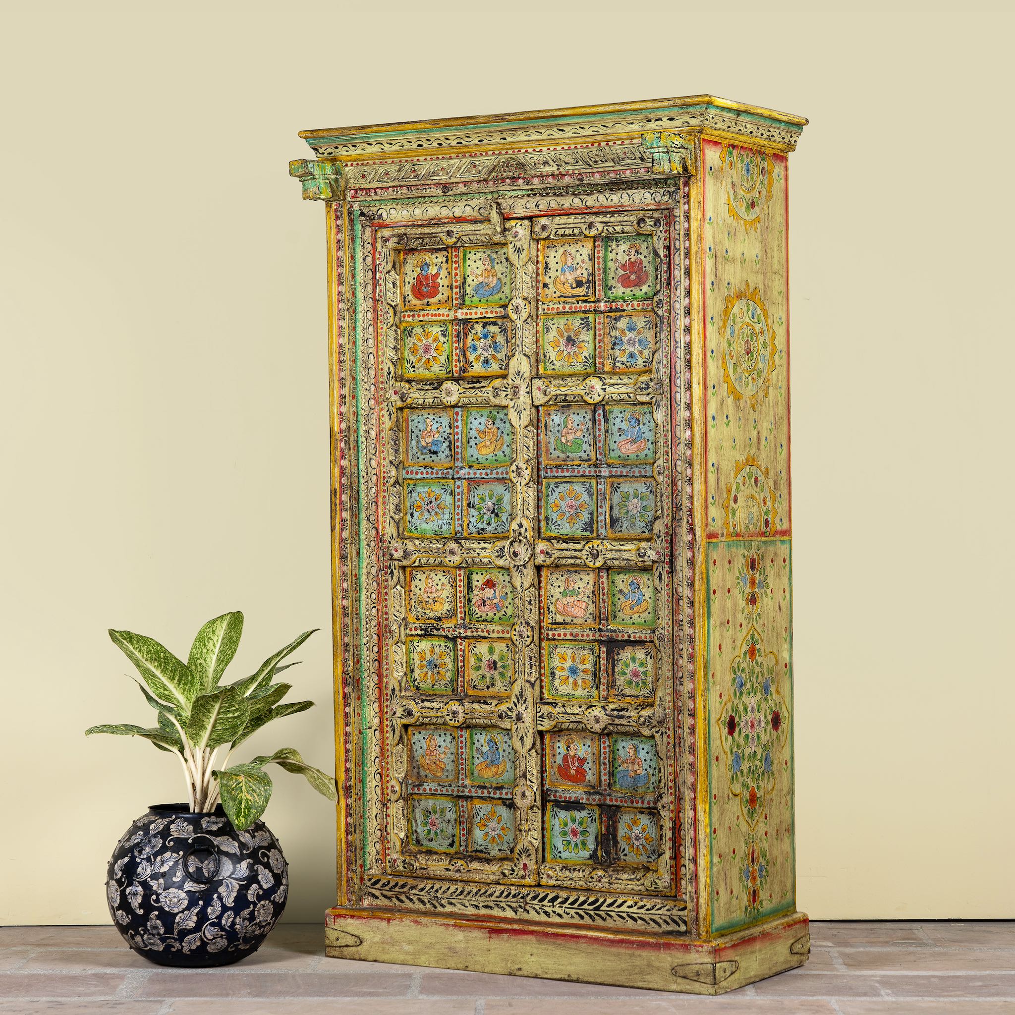 Side angle image of a hand painted wardrobe made of teak wood with floral motifs; unique furniture inspired by Indian artistry, 104 × 50 × 186 cm.