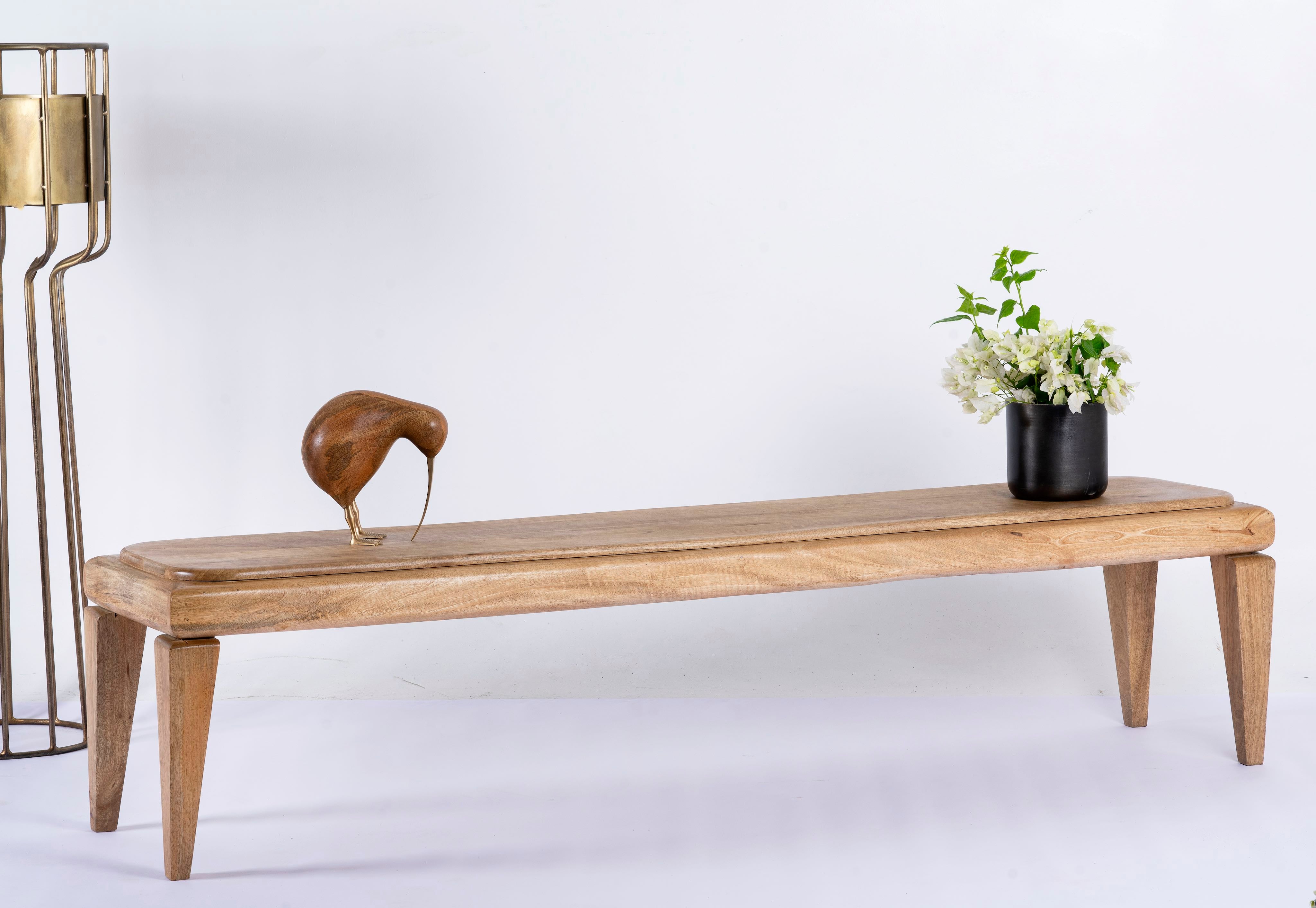 Side angle image of a minimalistic mango wood bench with natural finish and clean design; versatile wooden seating, 180 × 41 × 44 cm.