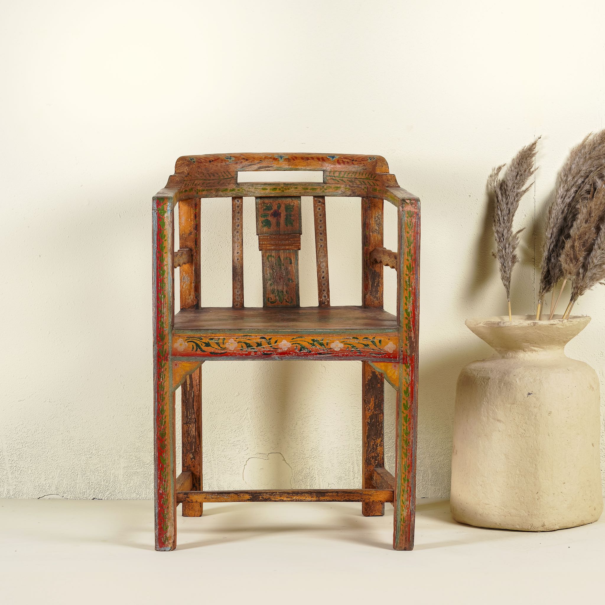Hand-painted armchair crafted from reclaimed teak wood, featuring intricate traditional patterns in earthy tones on the backrest, seat, and frame, with a rustic and vintage finish.