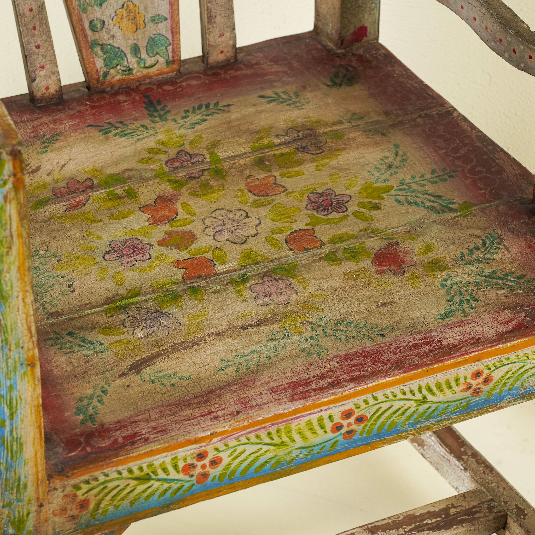 Close up image of the seating of a hand-painted armchair crafted from reclaimed teak wood, featuring intricate traditional patterns in earthy tones on the backrest, seat, and frame, with a rustic and vintage finish.