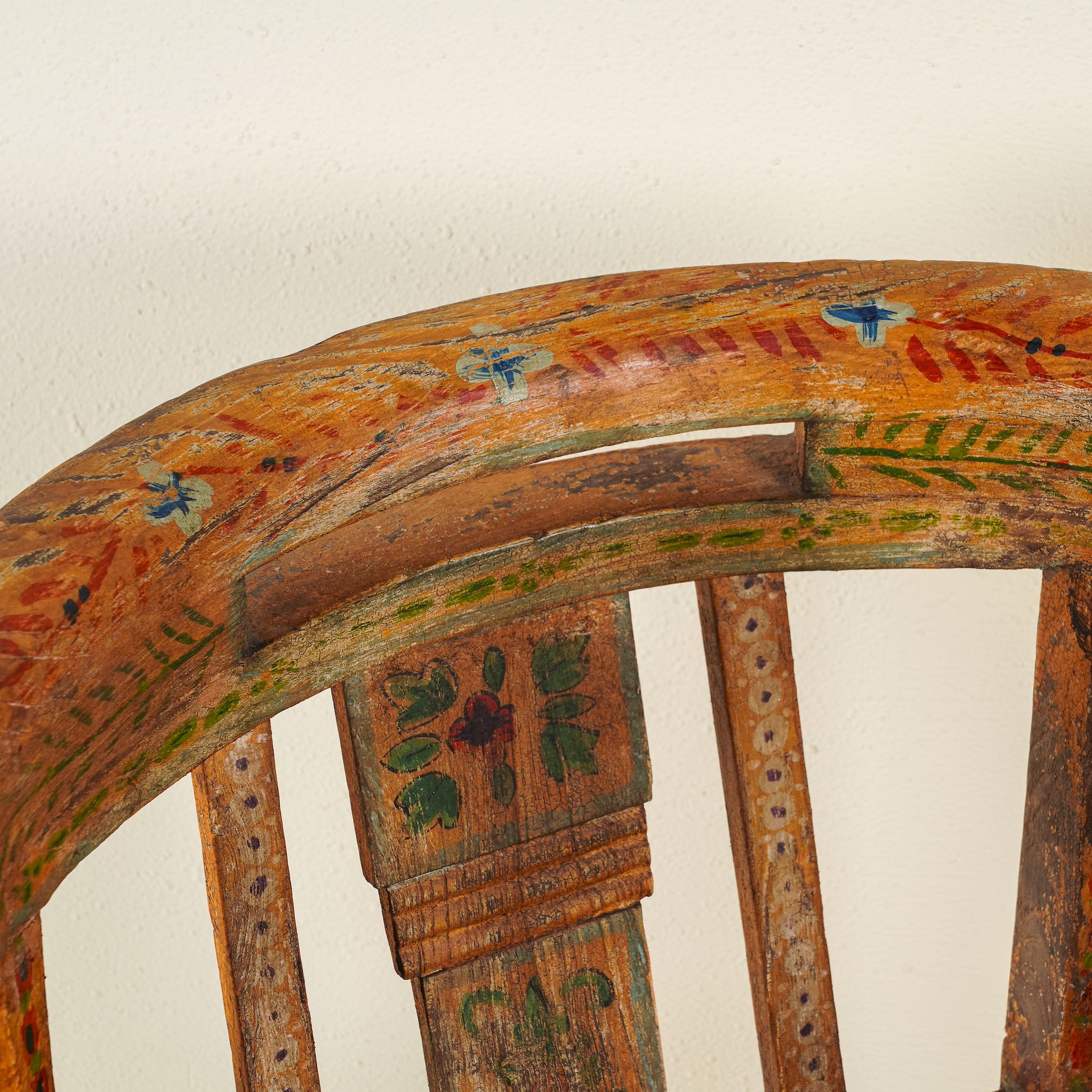 Close up image of the backrest of a hand-painted armchair crafted from reclaimed teak wood, featuring intricate traditional patterns in earthy tones on the backrest, seat, and frame, with a rustic and vintage finish.