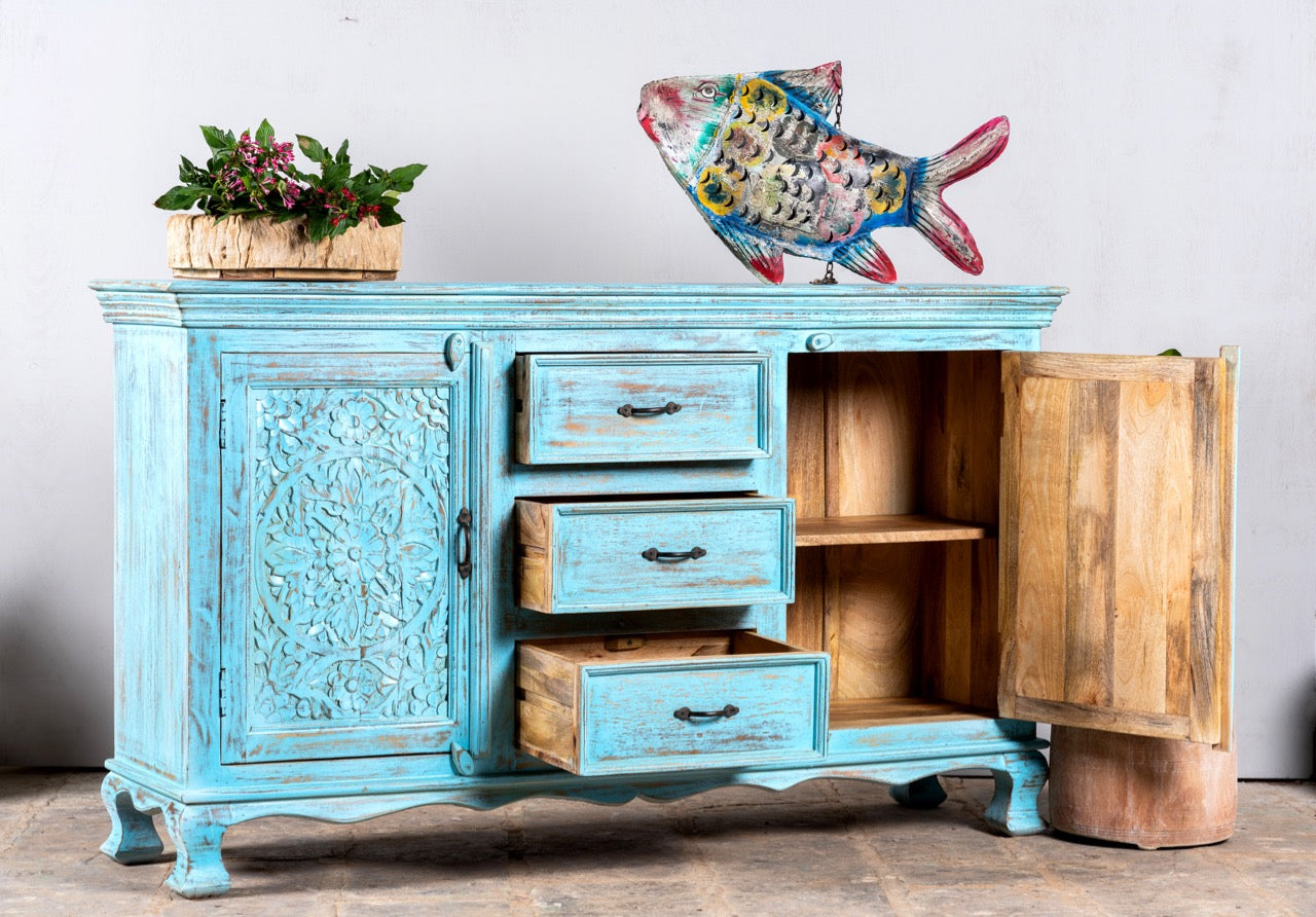 Side angle image with open drawers of a hand-carved mango wood sideboard with distressed blue wash finish, artisanal furniture for bohemian interior, 150 × 40 × 90 cm.