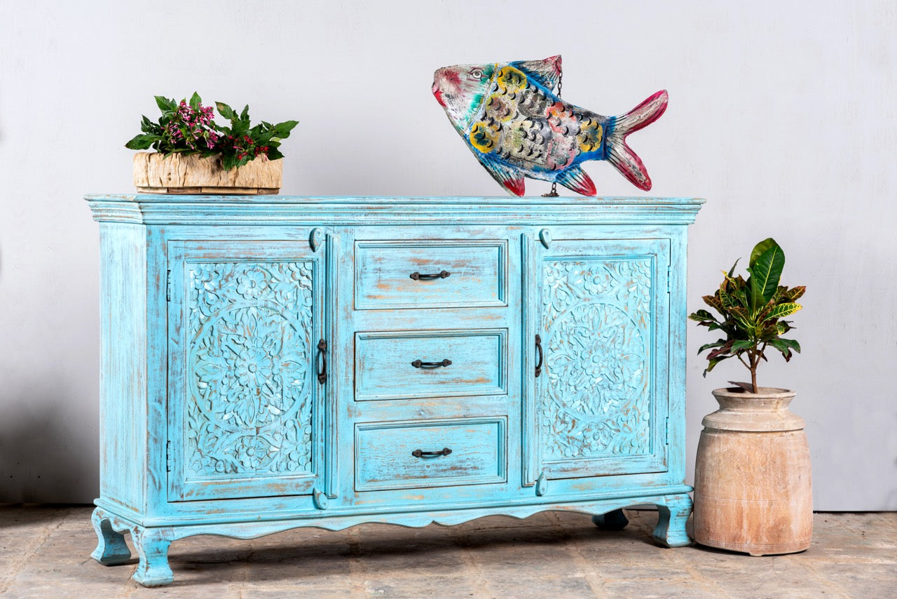 Side angle image of a Hand-carved mango wood sideboard with distressed blue wash finish, artisanal furniture for bohemian interior, 150 × 40 × 90 cm.