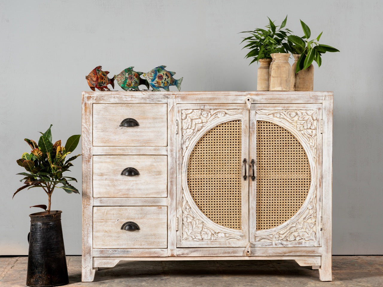 Life style image of a handcrafted mango wood dresser with floral carvings and rattan cane inserts, bohemian interior and rattan furniture style, whitewashed finish, 120 × 40 × 92 cm.