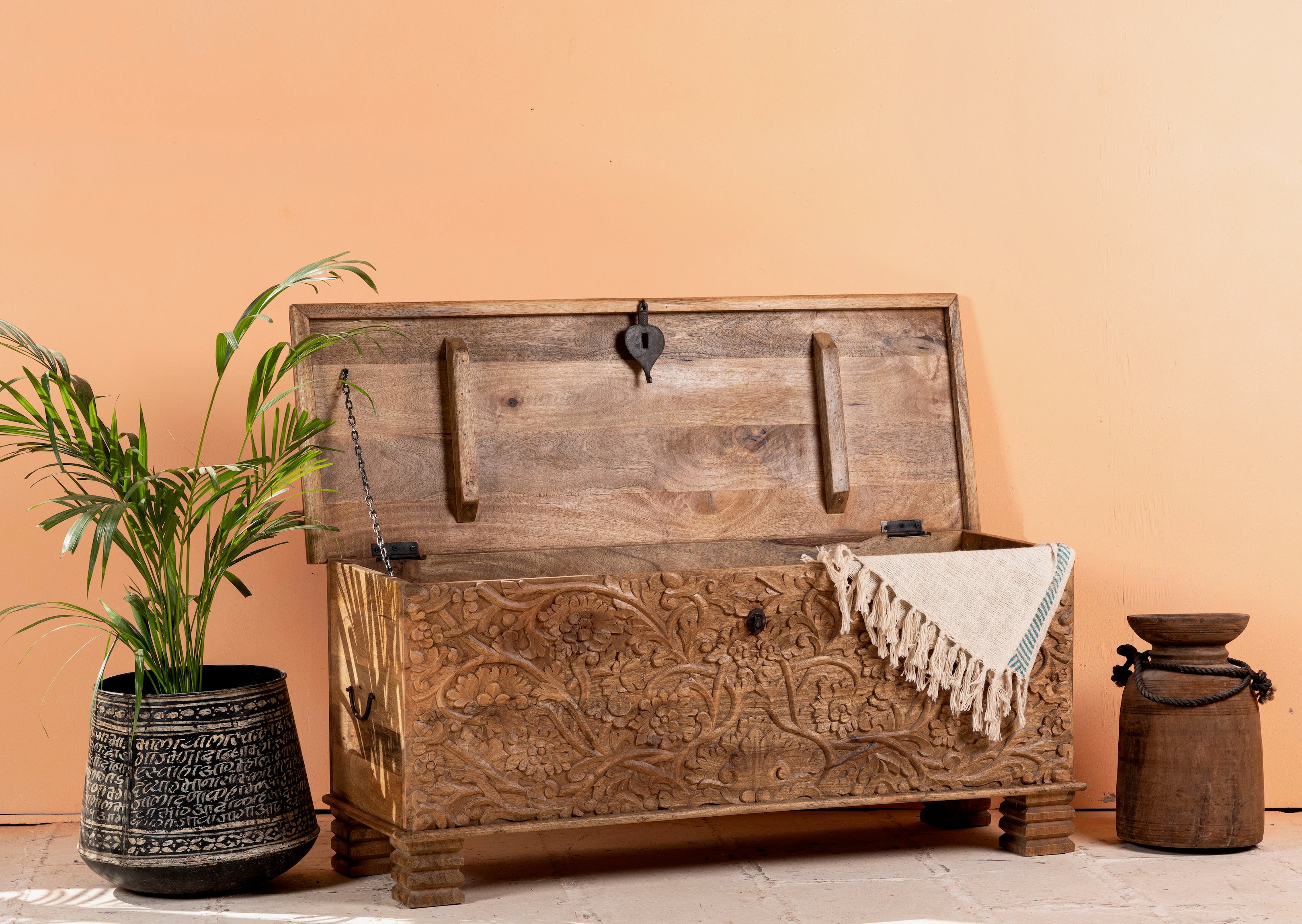 Side angle image with open lid of a hand-carved mango wood storage chest with floral detailing and iron fittings – wooden carved chest ideal for use as elegant bedroom furniture or storage.