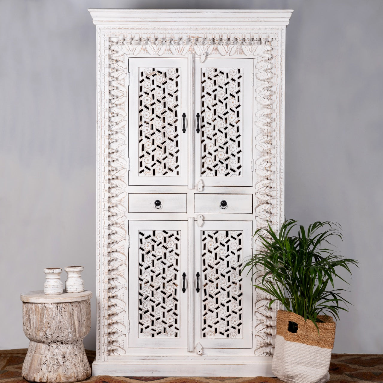 Lifestyle image of a hand-carved mango wood cabinet with shelving and whitewashed finish, bedroom furniture with floral and geometric motifs, 190 × 105 × 40 cm.