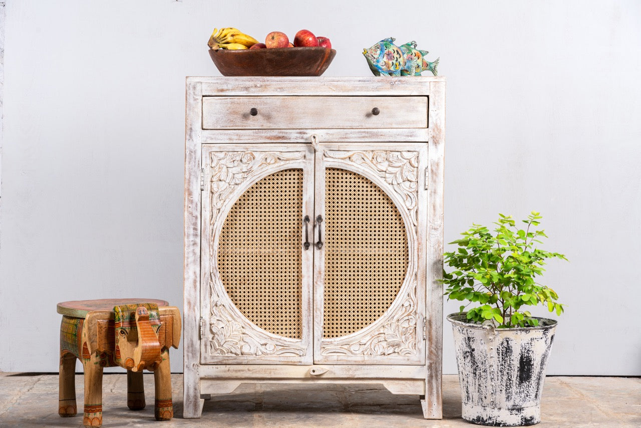 White‑washed mango wood cupboard with rattan door panels and hand‑carved Indian ornamentation, 80 × 40 × 104 cm.