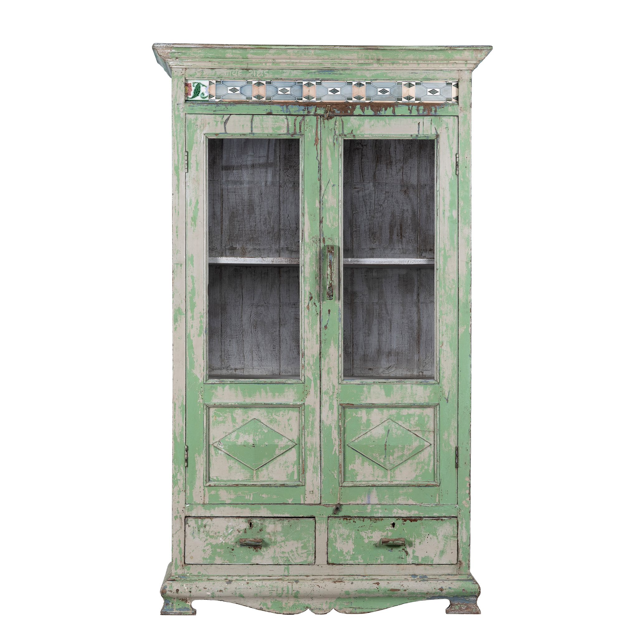 White background image of a reclaimed teak wood vitrine with distressed green finish, ceramic inlays, and glass-panelled doors – sustainable furniture with vintage Indian charm.