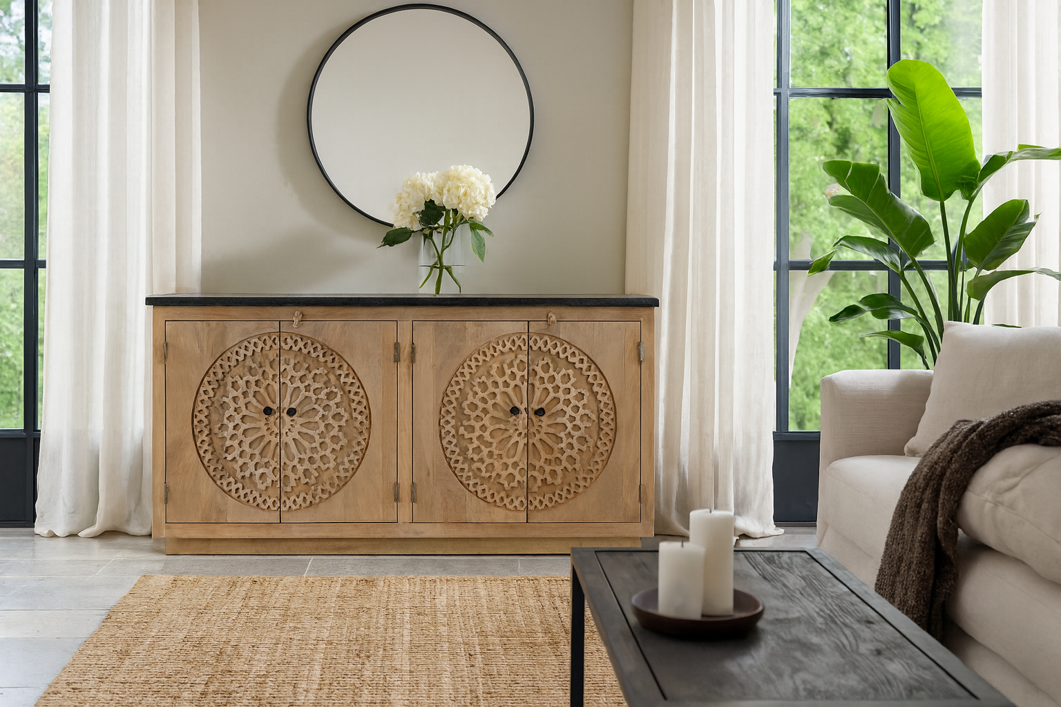 Wooden sideboard with decorative carvings in a living room setting with a mirror, flowers, and a couch.