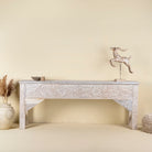 Front view image of a hand carved console table made from reclaimed wood, showcasing an ornate floral design with a whitewashed finish that highlights the intricate details and natural imperfections of the repurposed material.
