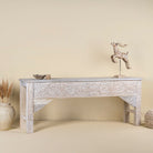 Side angle image of a handcarved console table made from reclaimed wood, showcasing an ornate floral design with a whitewashed finish that highlights the intricate details and natural imperfections of the repurposed material.
