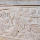 Close up image of a handcarved console table made from reclaimed wood, showcasing an ornate floral design with a whitewashed finish that highlights the intricate details and natural imperfections of the repurposed material.
