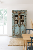 Lifestyle image of a reclaimed teak wood display cabinet with light blue shabby chic finish and ceramic inlays – sustainable teak wood showcase with glass doors.