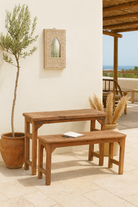 Lifestyle image of a teak wood bench set made from refurbished wood with hand-carved detailing and rustic finish, 120 × 30 × 65 cm.