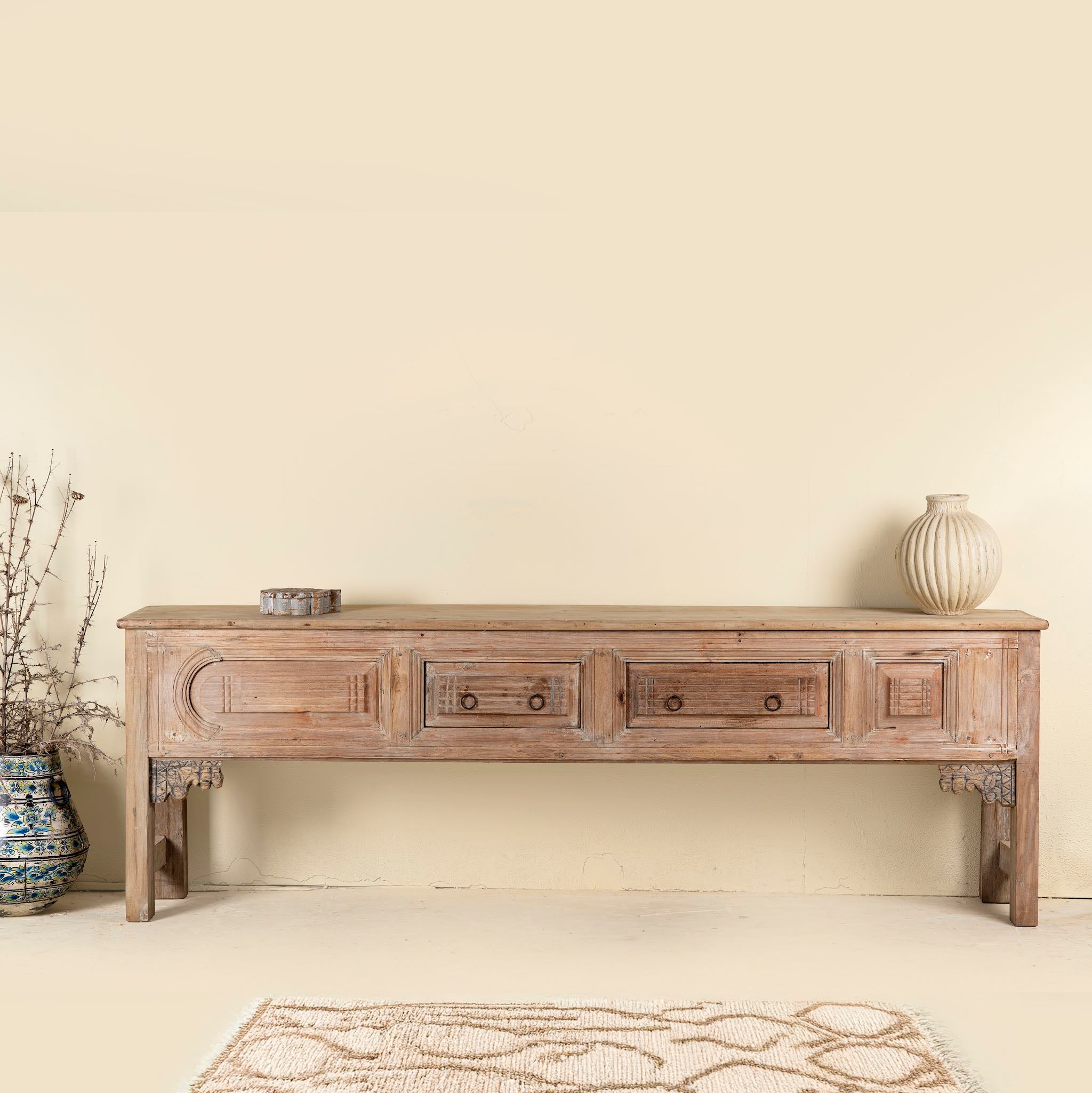 Antique console table crafted from aged teak wood, featuring detailed hand carvings, two central drawers, and a weathered patina for timeless character.